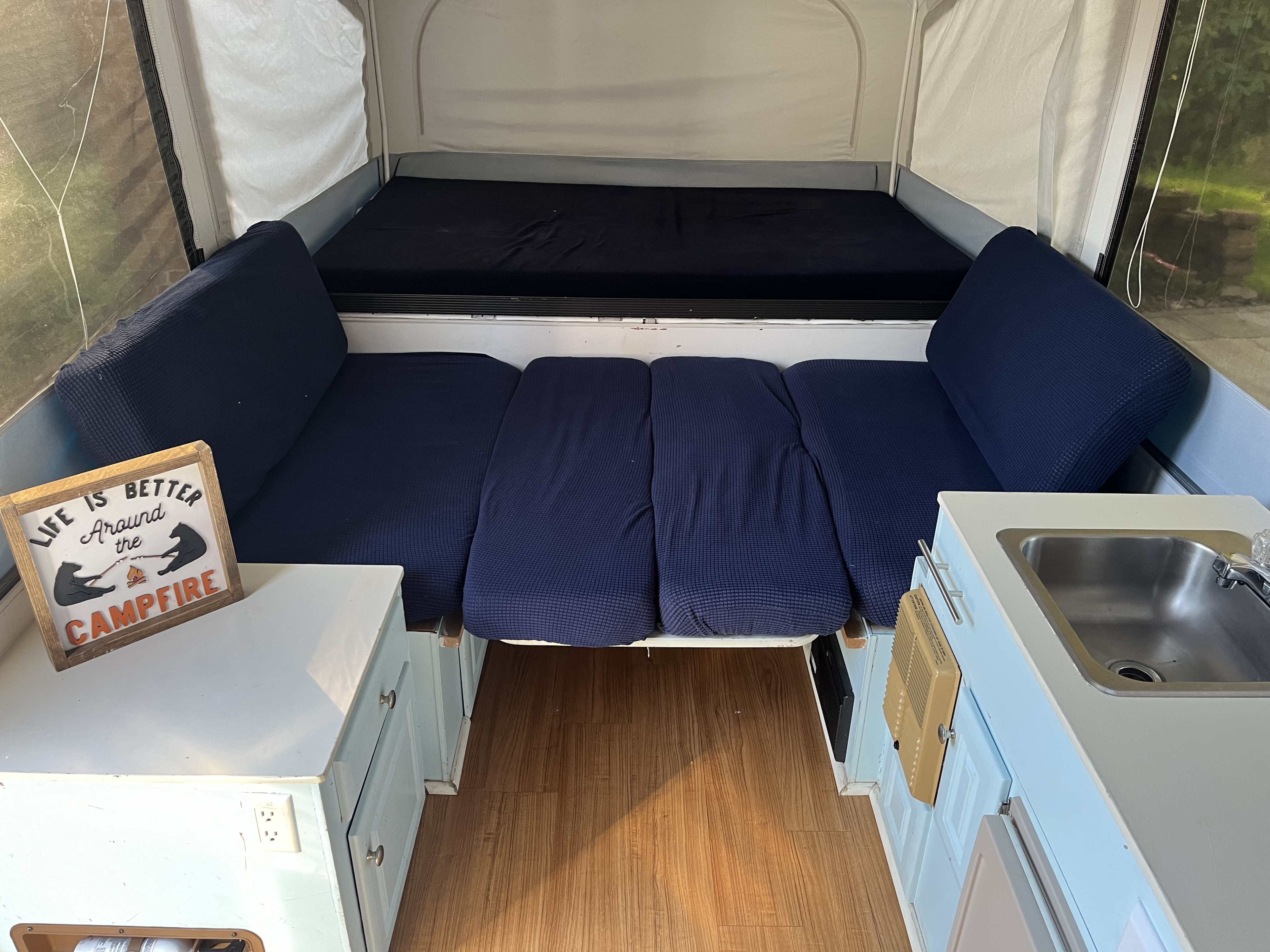 Inside a pop-up RV rental, showcasing blue beds, a compact kitchen sink, wooden floor, and a 'campfire' sign.. Jayco Jay 2007