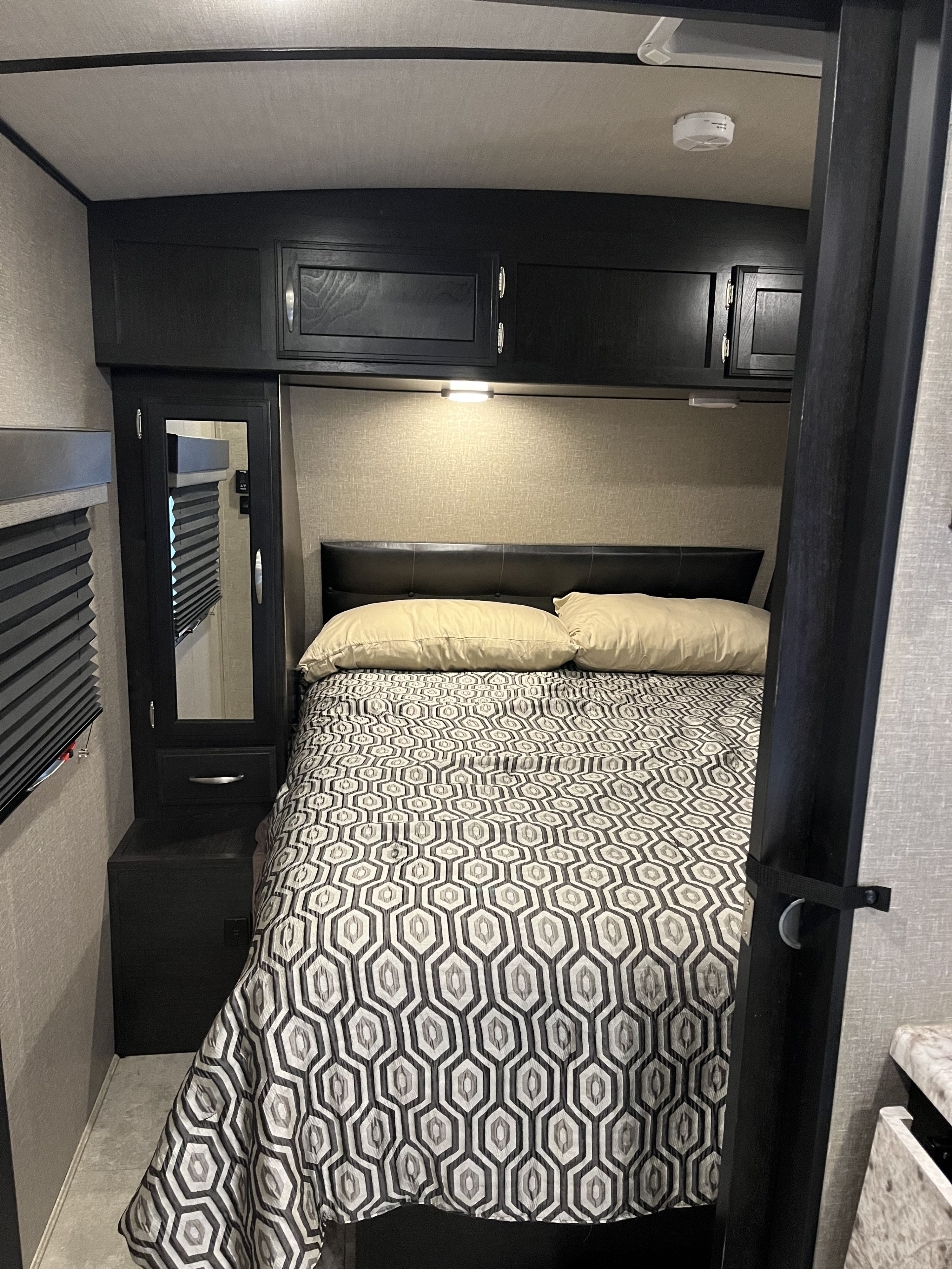 Cozy RV rental bedroom with a geometric patterned bed, overhead cabinets, and mirror. Ideal for a camper's retreat.. Grand Design Imagine 2020