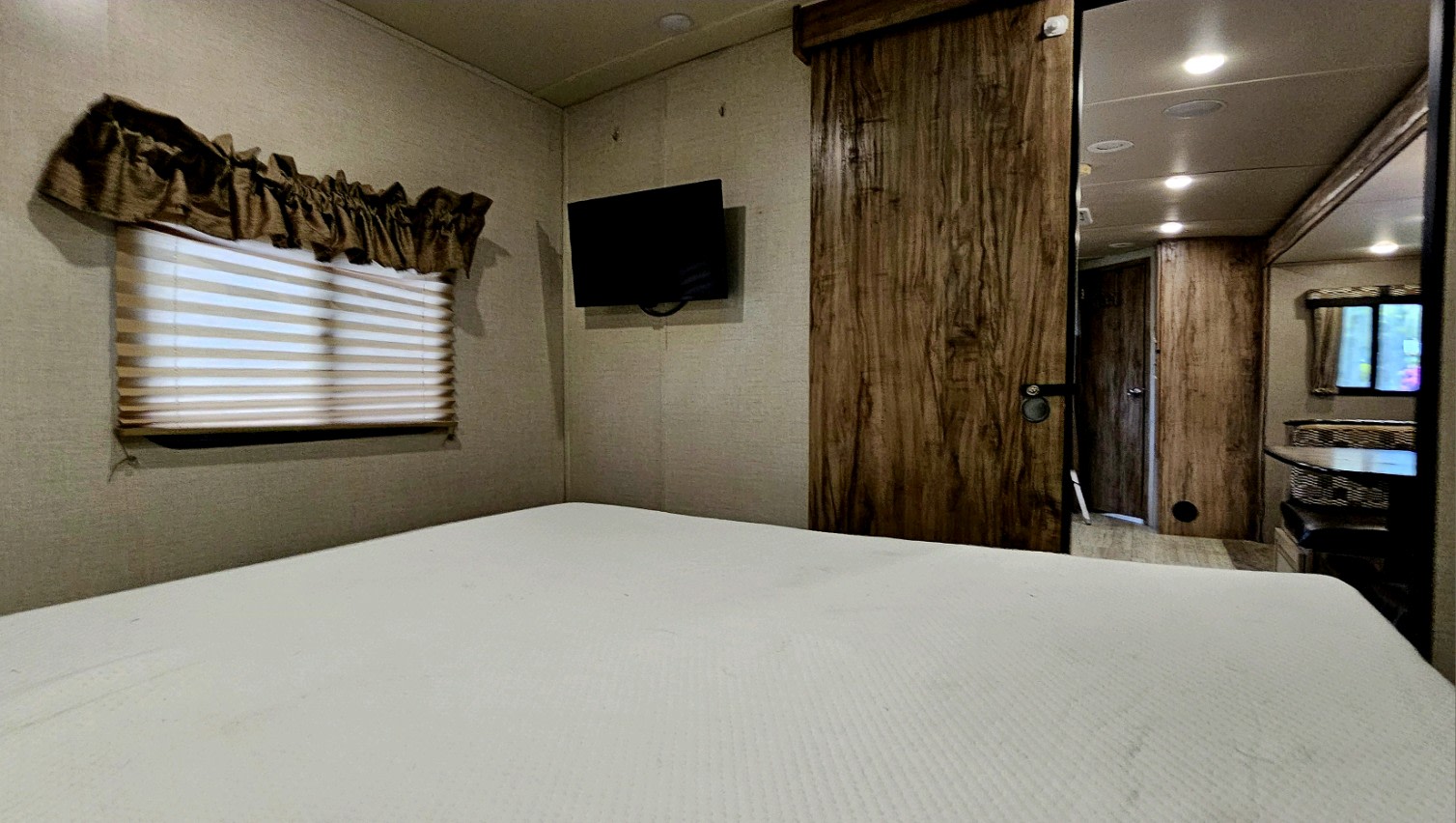 Inside an rv rental, a bedroom features a large bed, wall-mounted TV, and a window with blinds and valance.. Palomino Solaire 268 BHSK 2020