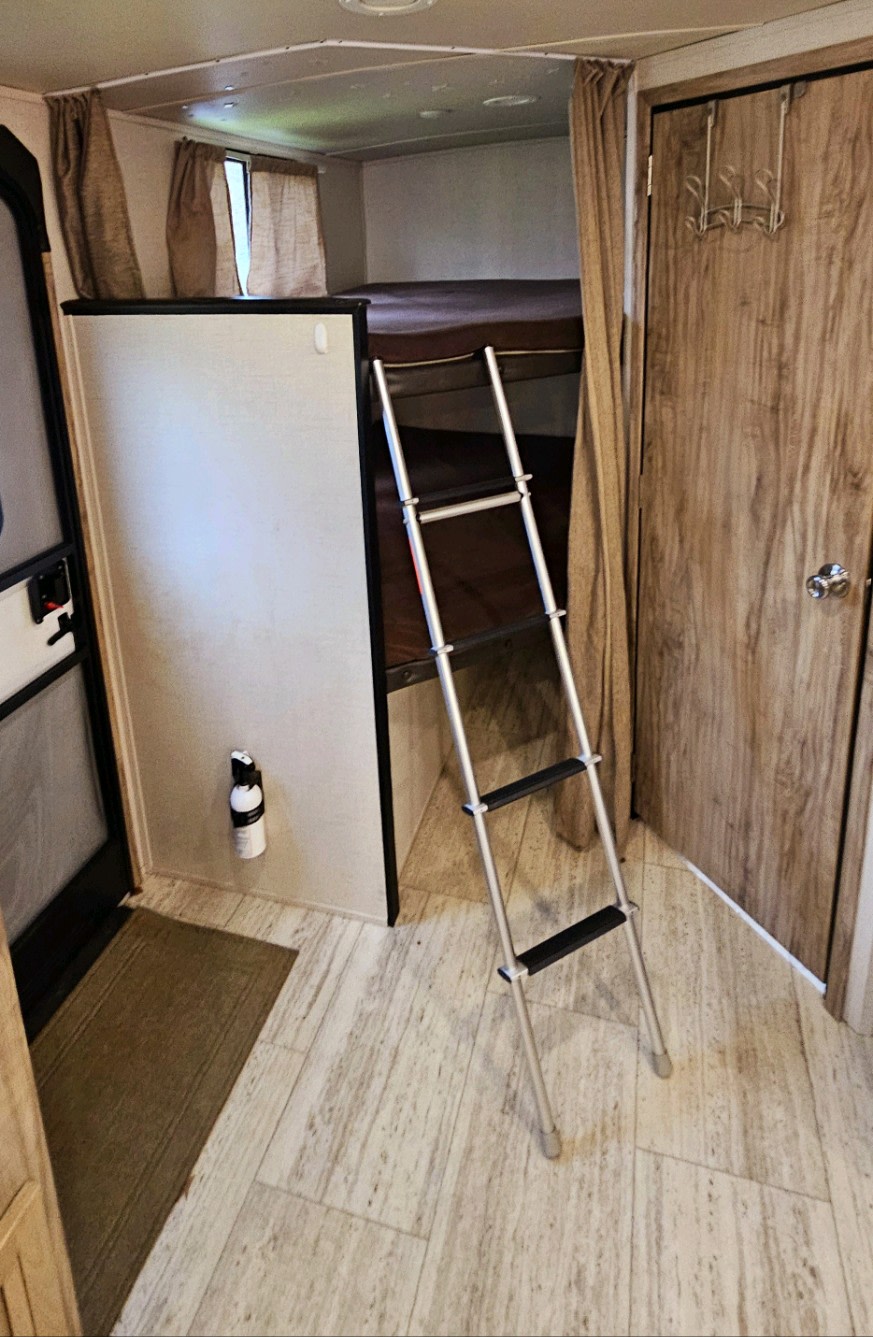 RV rental interior shows bunk beds with a ladder, a nearby door with hooks, and a wall-mounted fire extinguisher.. Palomino Solaire 268 BHSK 2020