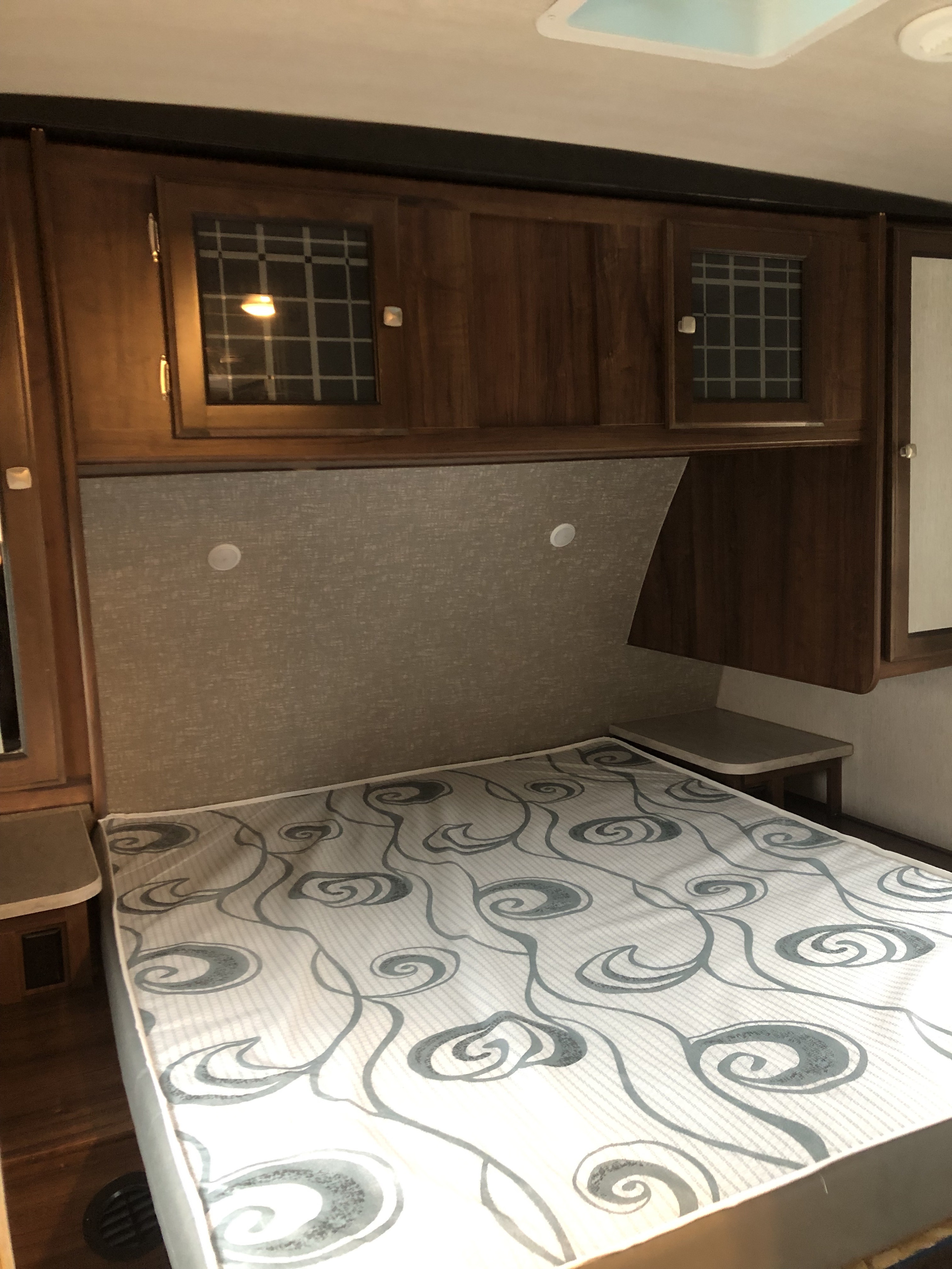 Compact RV rental bedroom featuring a patterned bed, wood cabinetry, and built-in side tables. Ideal for travel.. Heartland RVs Wilderness 2019