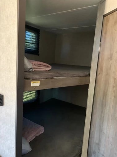 RV rental bunk beds: A practical sleeping area with upper and lower bunks, mattresses, and pink blankets. Window visible.. Dutchmen Coleman 420LH 2020