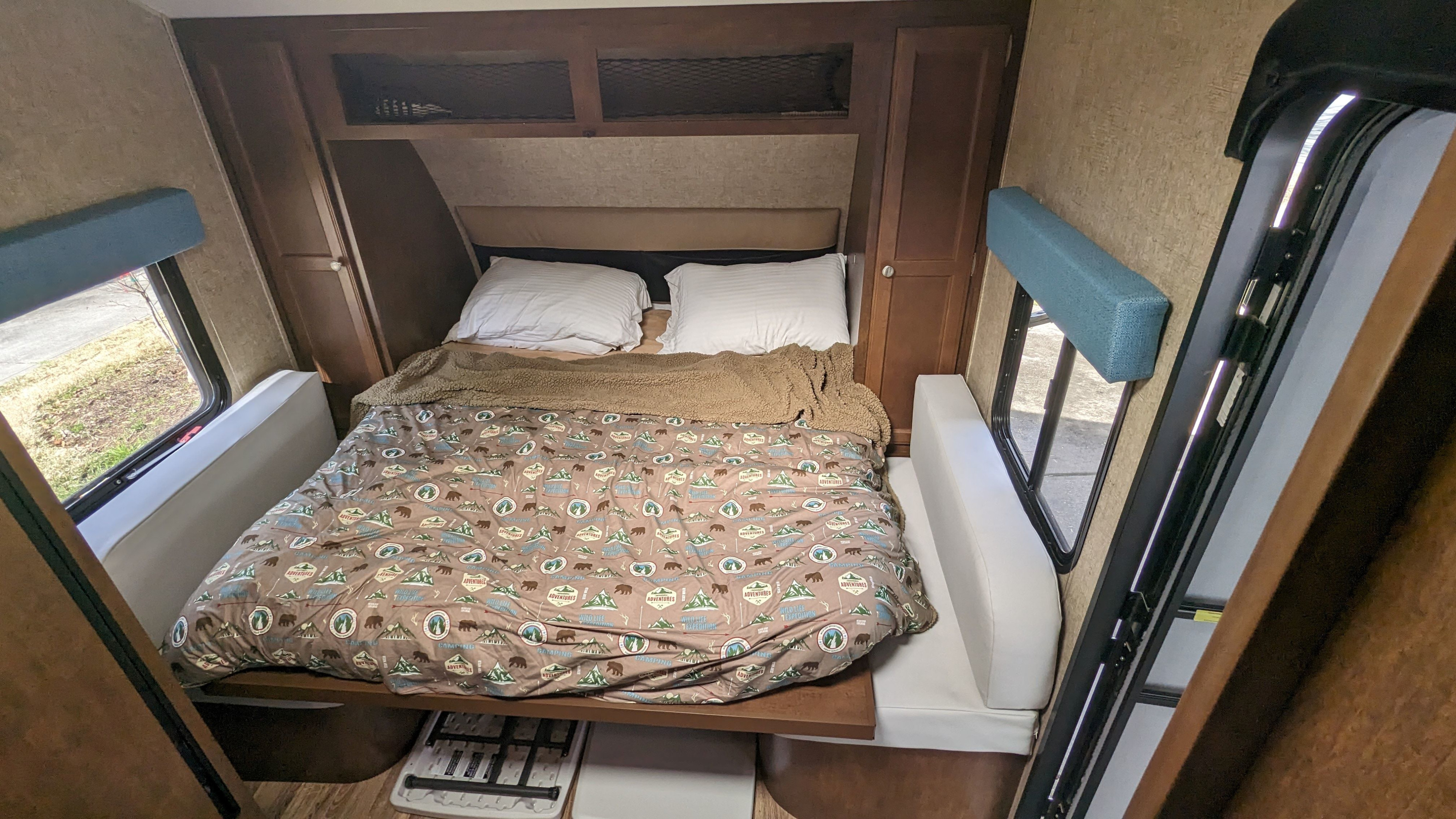 Compact RV rental bedroom with camping-themed bedding, side storage, and windows, ideal for mobile adventures.. Sonic Lite 2016