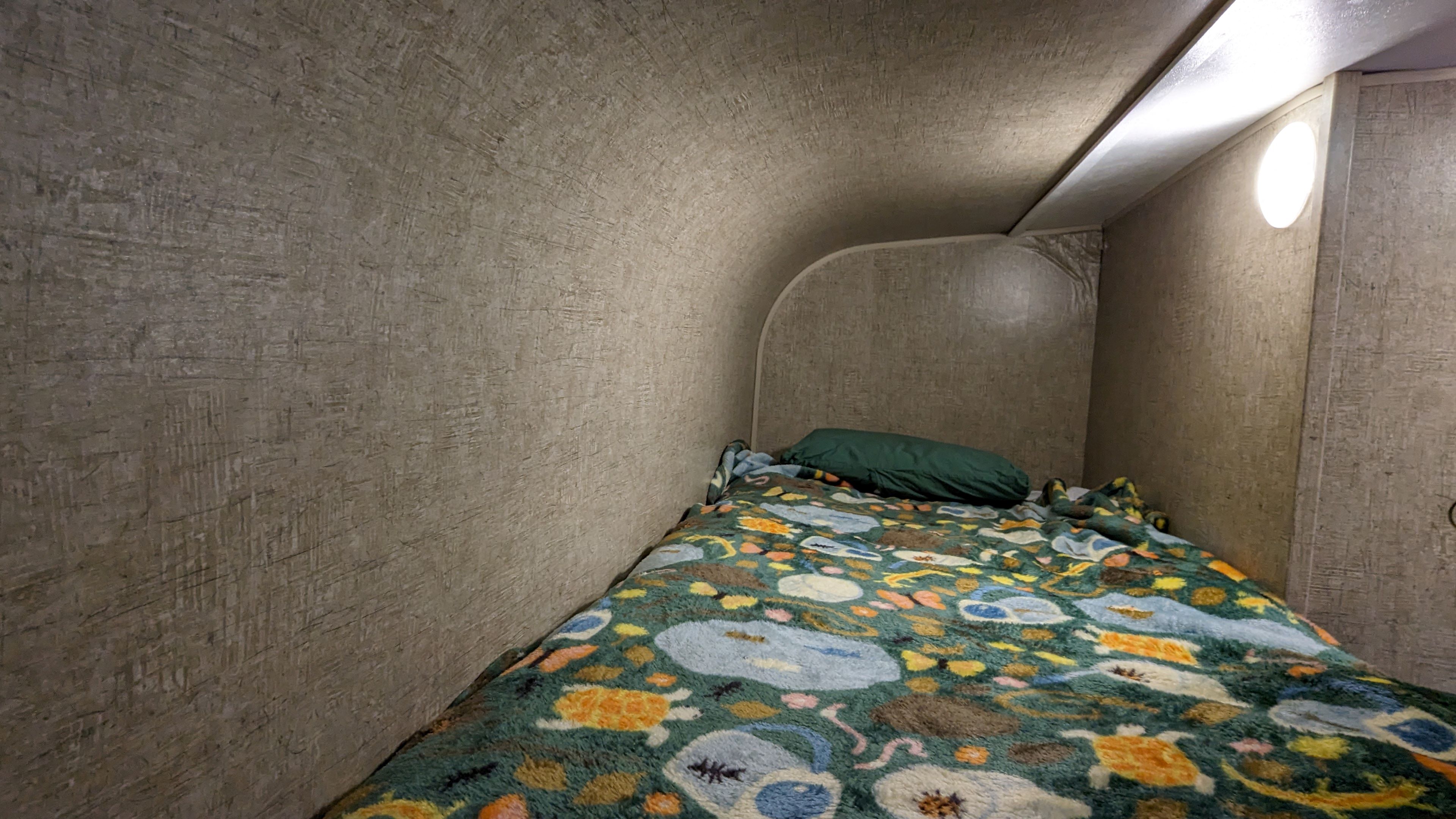 Inside an rv rental, a compact bunk bed with a colorful animal-themed blanket and green pillow provides a cozy sleeping space.. Sonic Lite 2016