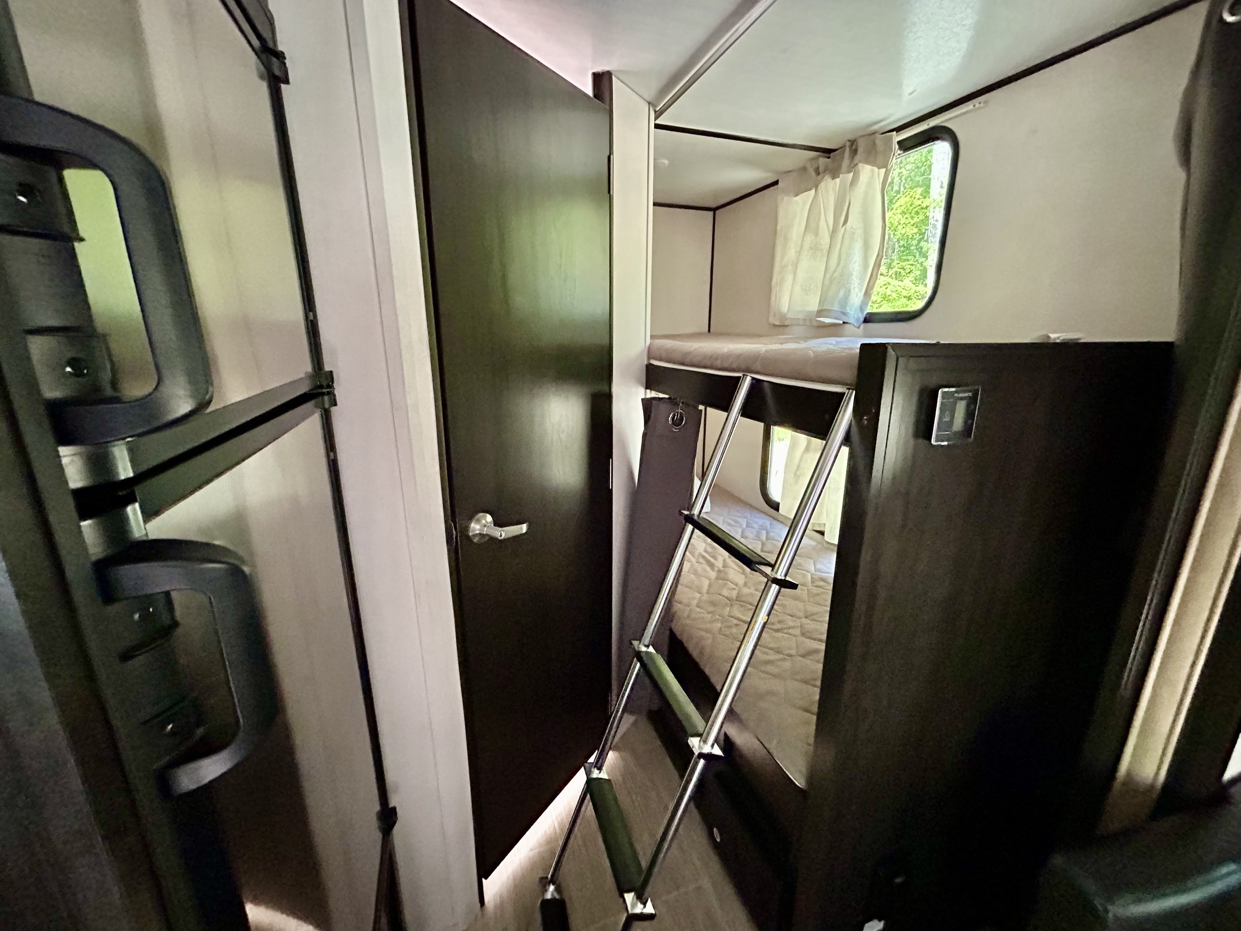 RV rental's cozy interior featuring bunk beds with a ladder. A window view of trees completes this compact space.. Forest River Surveyor Legend 2019