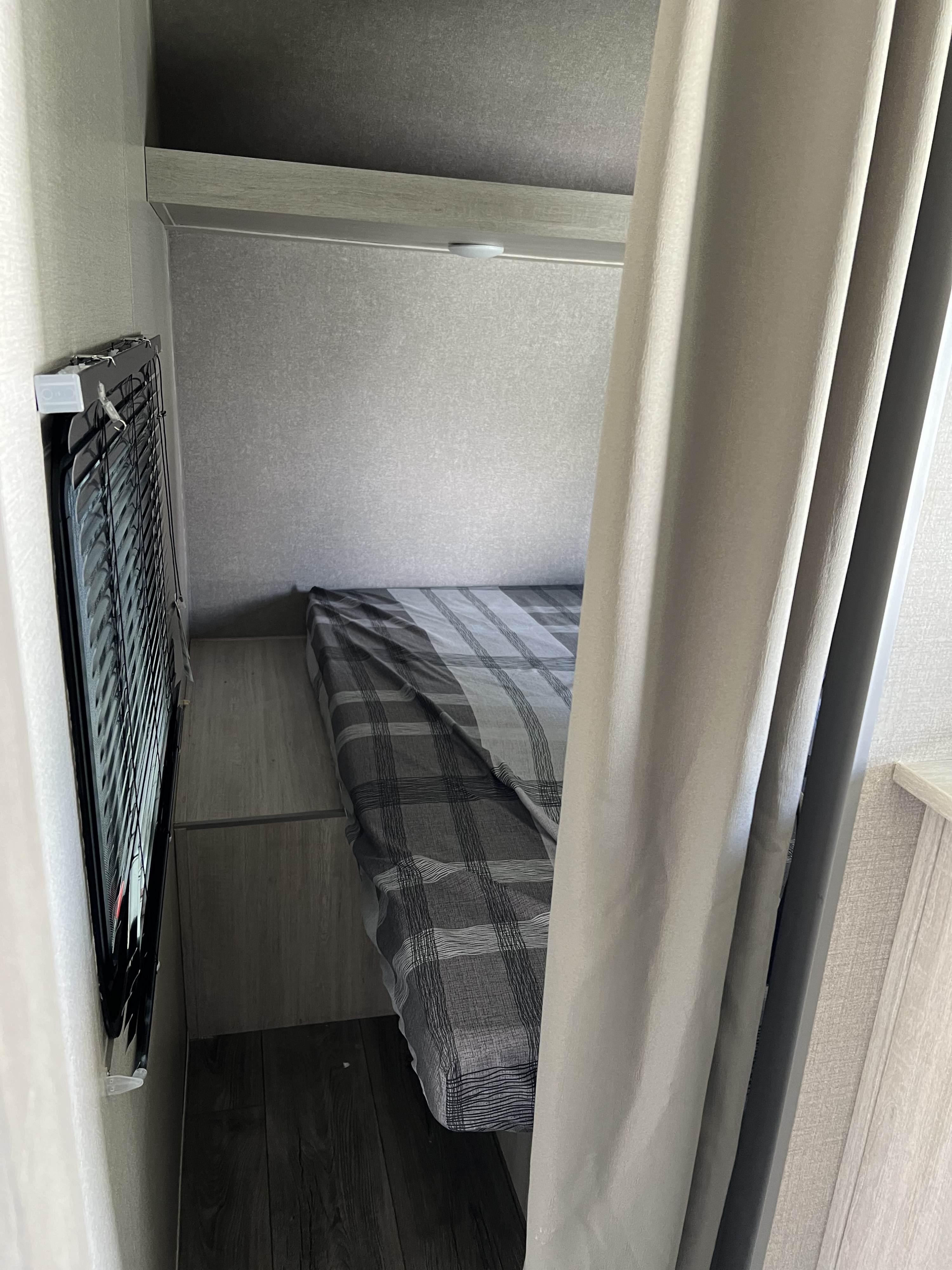 This RV rental offers a cozy bedroom area with a plaid bed, window blinds, and privacy curtain.. Coachmen Catalina 2022