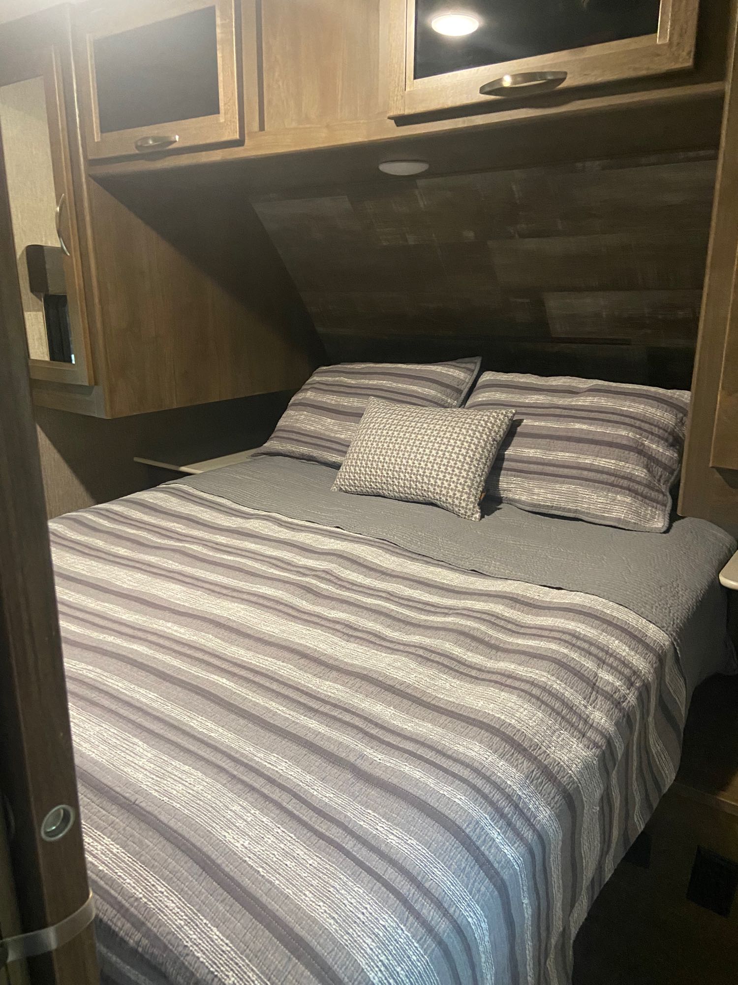 Cozy RV rental bedroom with striped bedding and overhead storage.. Dutchmen Coleman Light 2019