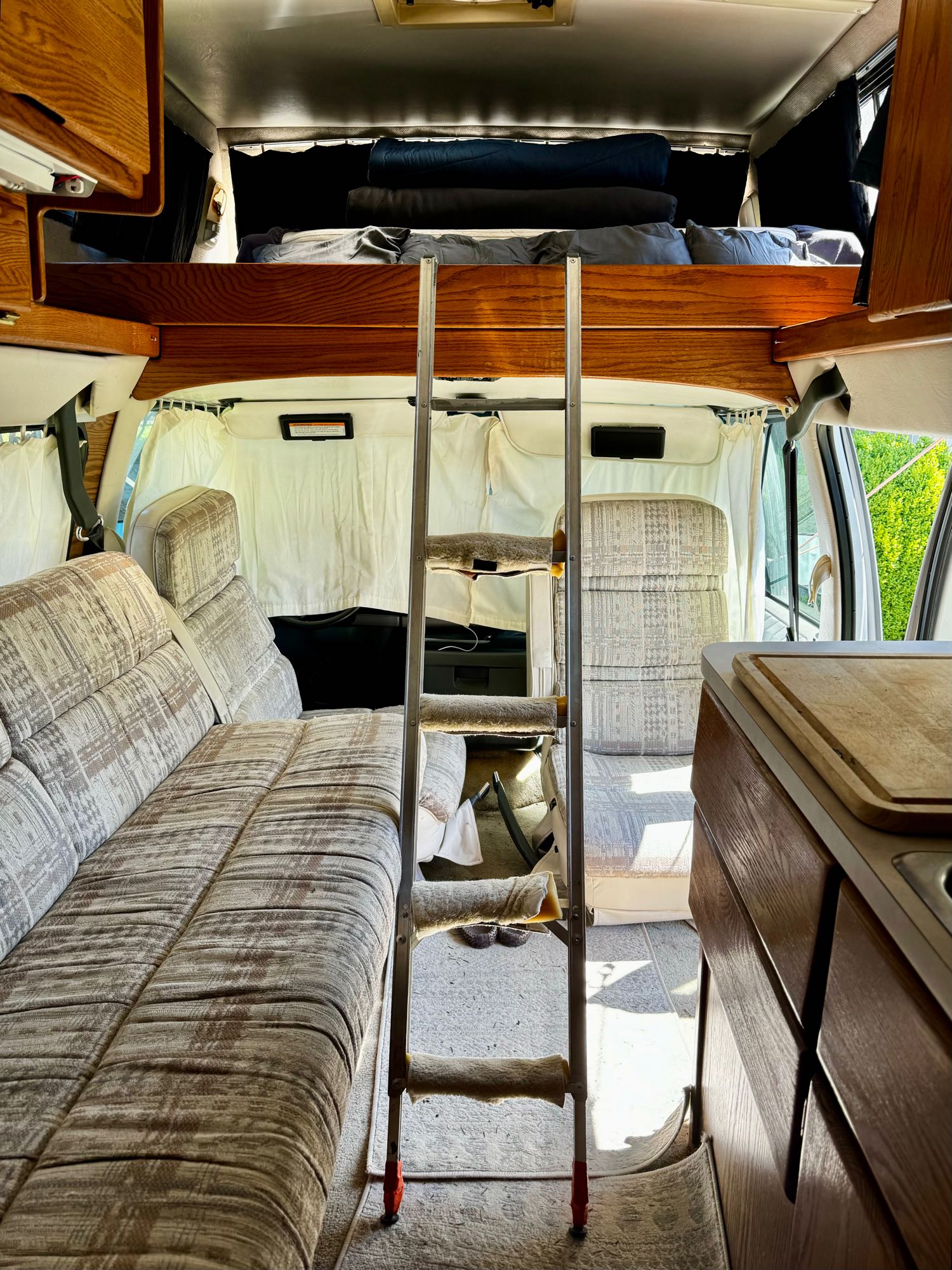 Cozy RV rental interior featuring a ladder leading to an overhead bunk, sofa seating, and a compact kitchen counter.. Ford Airstream B190 1996