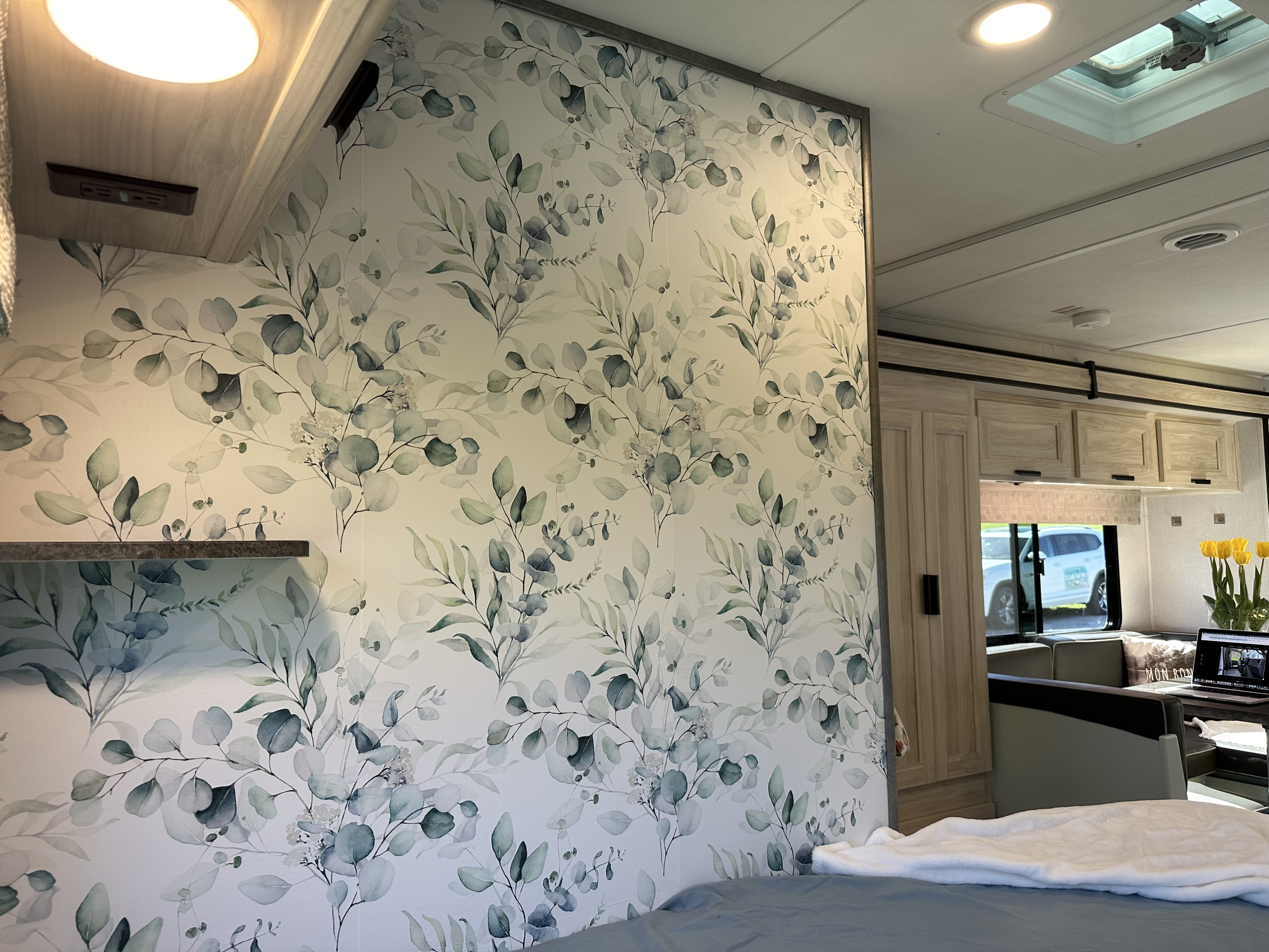RV rental bedroom with stylish eucalyptus leaf wallpaper and cozy bed, opening to a bright living area.. Forest River Sunseeker LE 2023