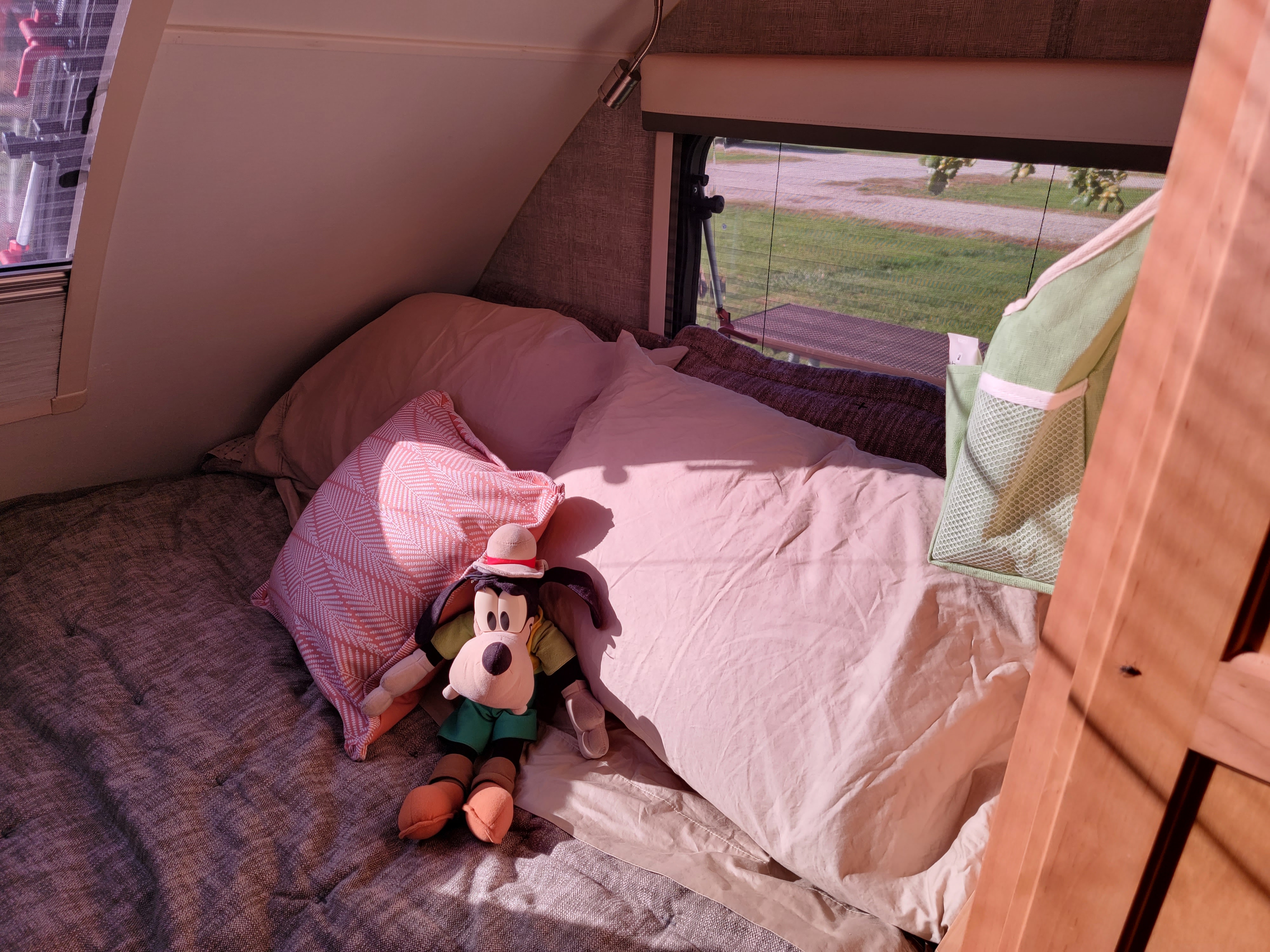 Sunny RV rental bedroom showing a cozy bed, Goofy plush, and window view of the campsite.. Xtreme Outdoors Little Guy Max 2021