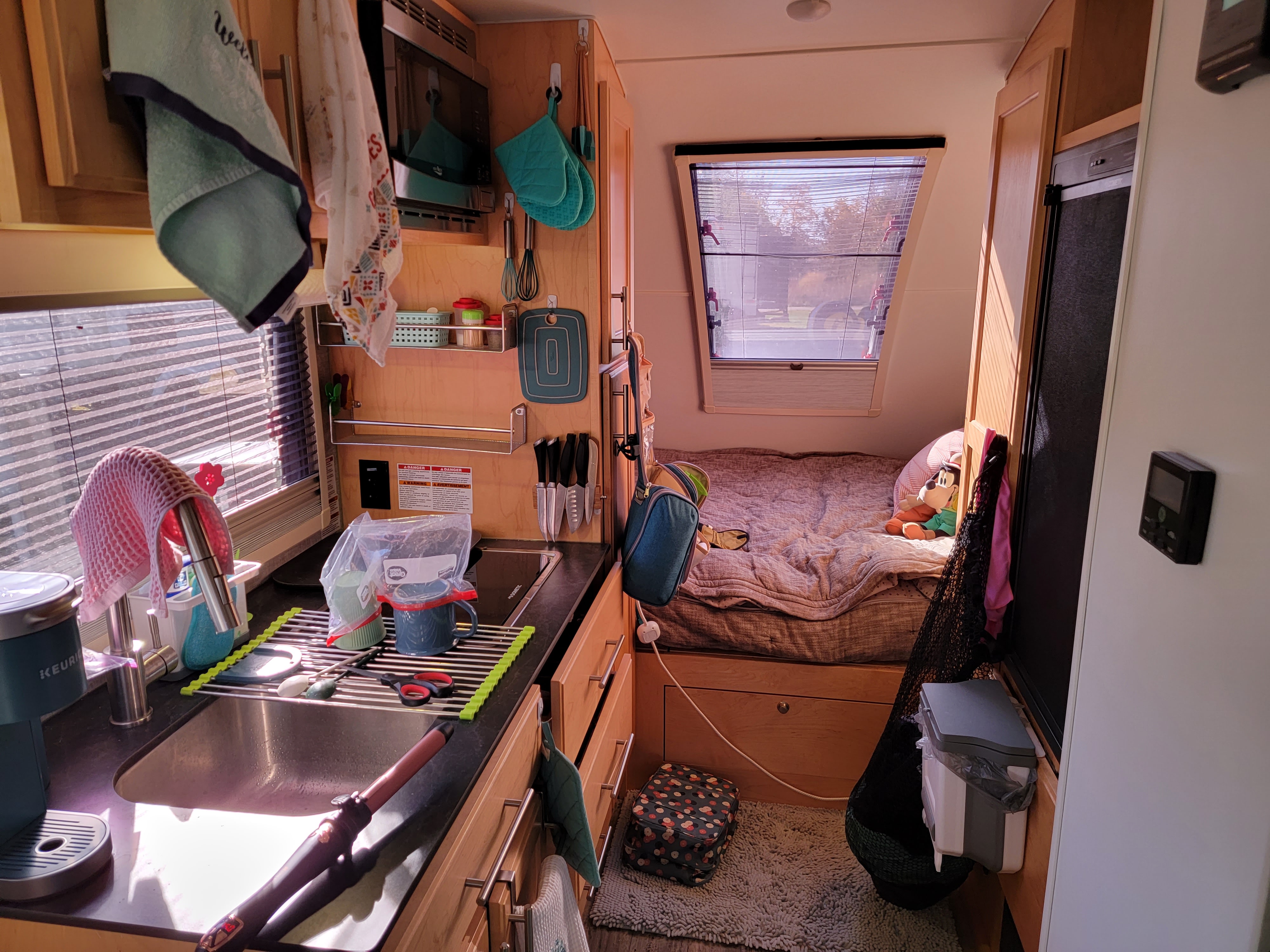Inside a bright RV rental: compact kitchen with sink, microwave, and a cozy bed for travel adventures.. Xtreme Outdoors Little Guy Max 2021