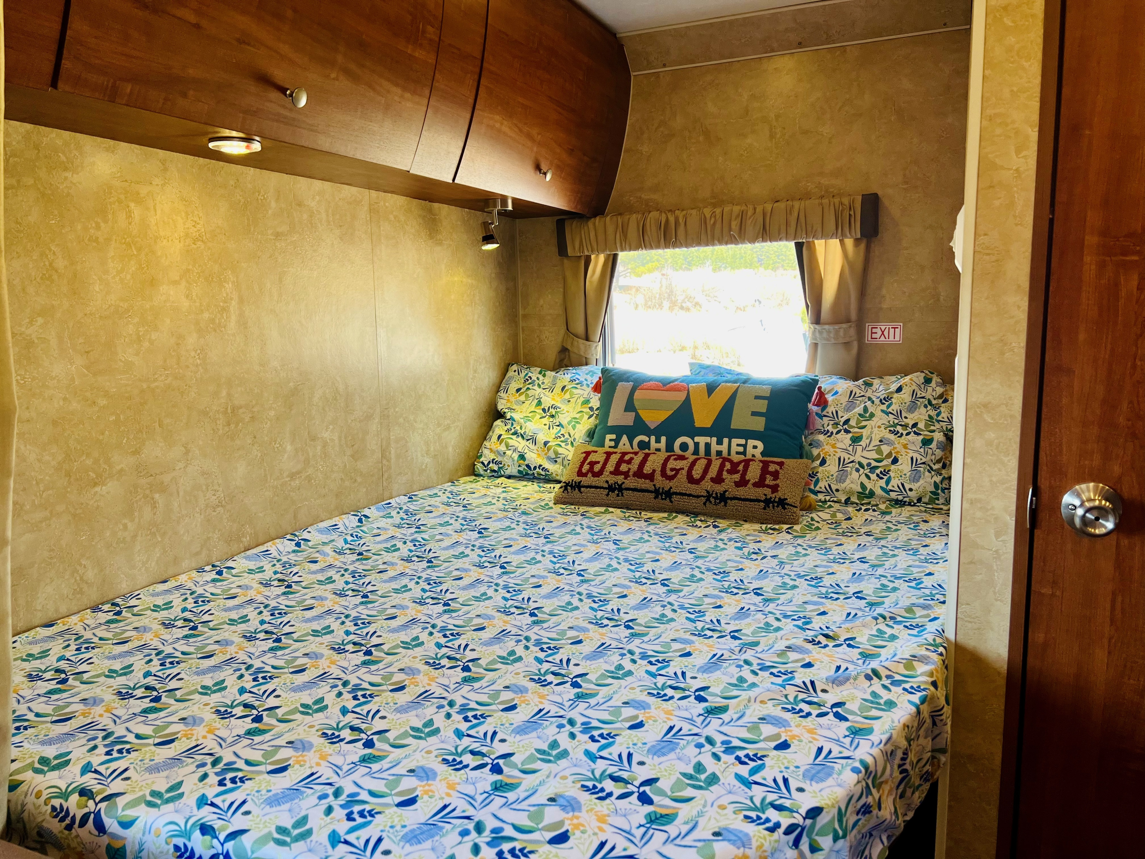 An inviting RV rental bedroom features a bed with vibrant floral sheets, cozy pillows, and warm wooden overhead cabinets.. Jayco Skylark 2011