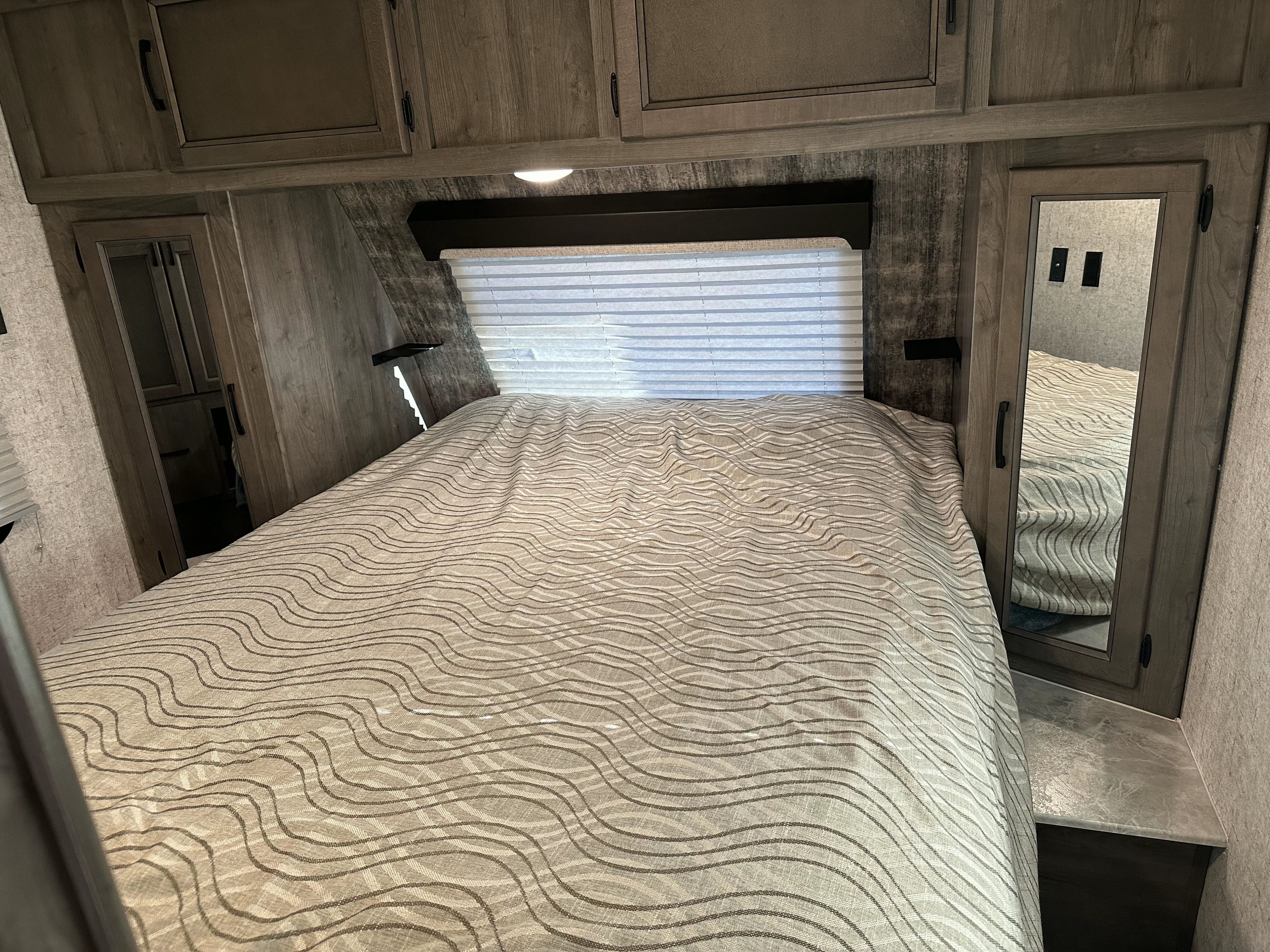 Cozy RV rental bedroom with a comfortable bed, overhead storage, reading lights, and a mirrored cabinet for your adventures.. Coachmen Apex 2020