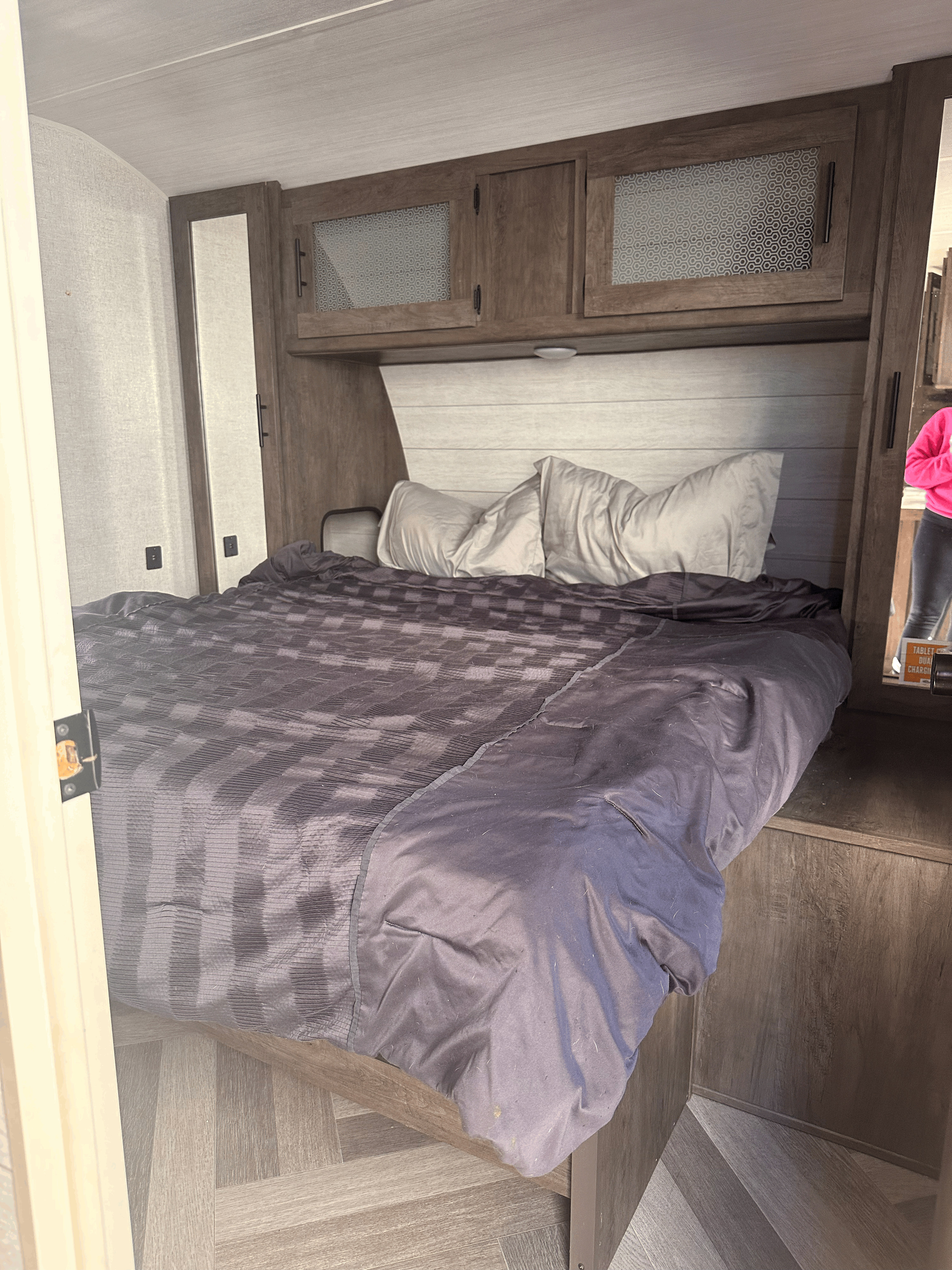 RV rental bedroom with a compact bed, dark bedding, overhead wood cabinets, and light wood-look flooring.. Forest River Salem 2020