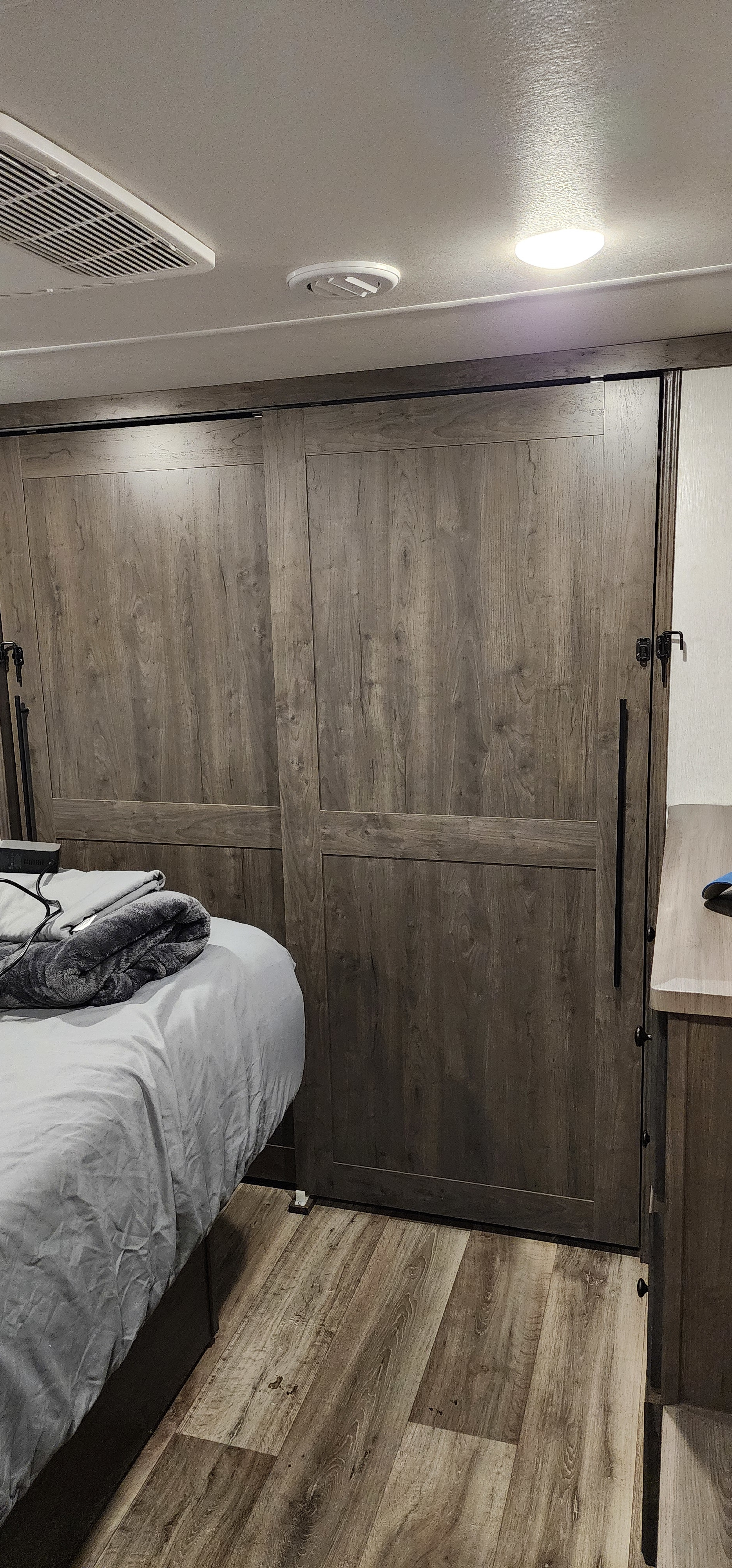RV rental master bedroom features modern wood-grain sliding doors, a comfy bed, and ceiling ventilation/lighting.. Forest River Cardinal Limited 2021