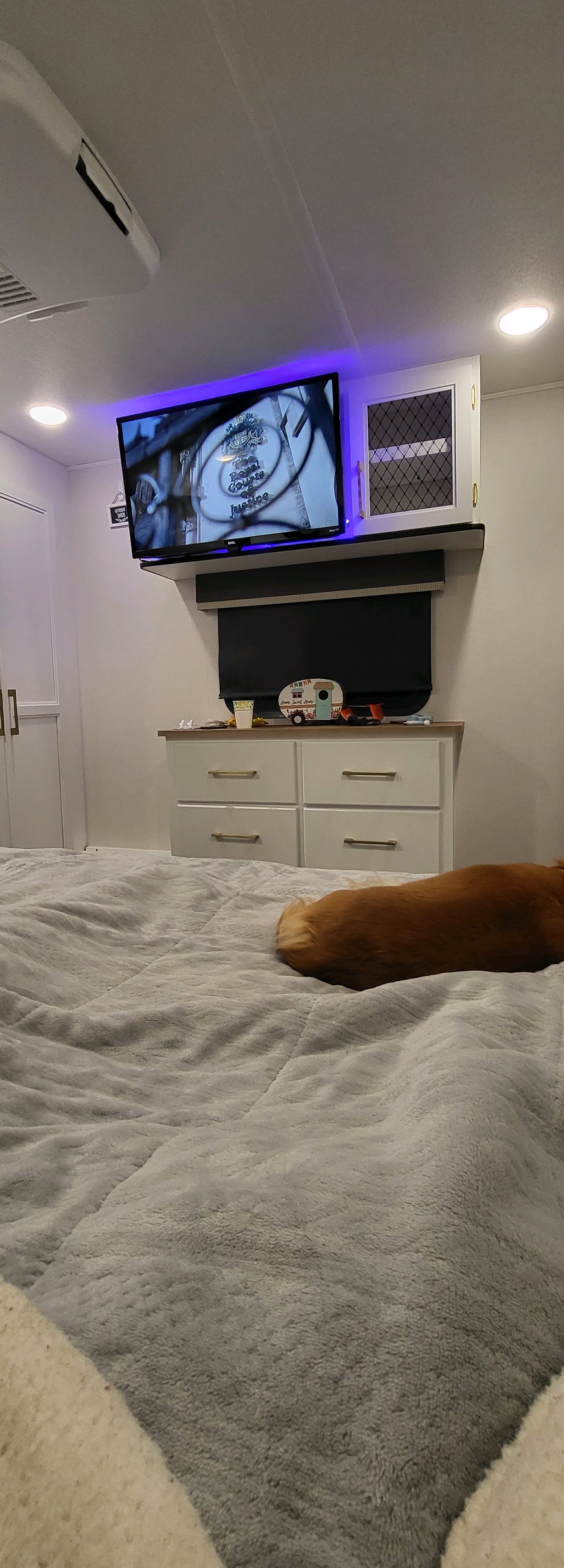 Inside an RV rental: A wall-mounted TV with purple backlighting, dresser, and a dog curled on the soft grey bed.. Crusader Crusader Fifth Wheel 2022