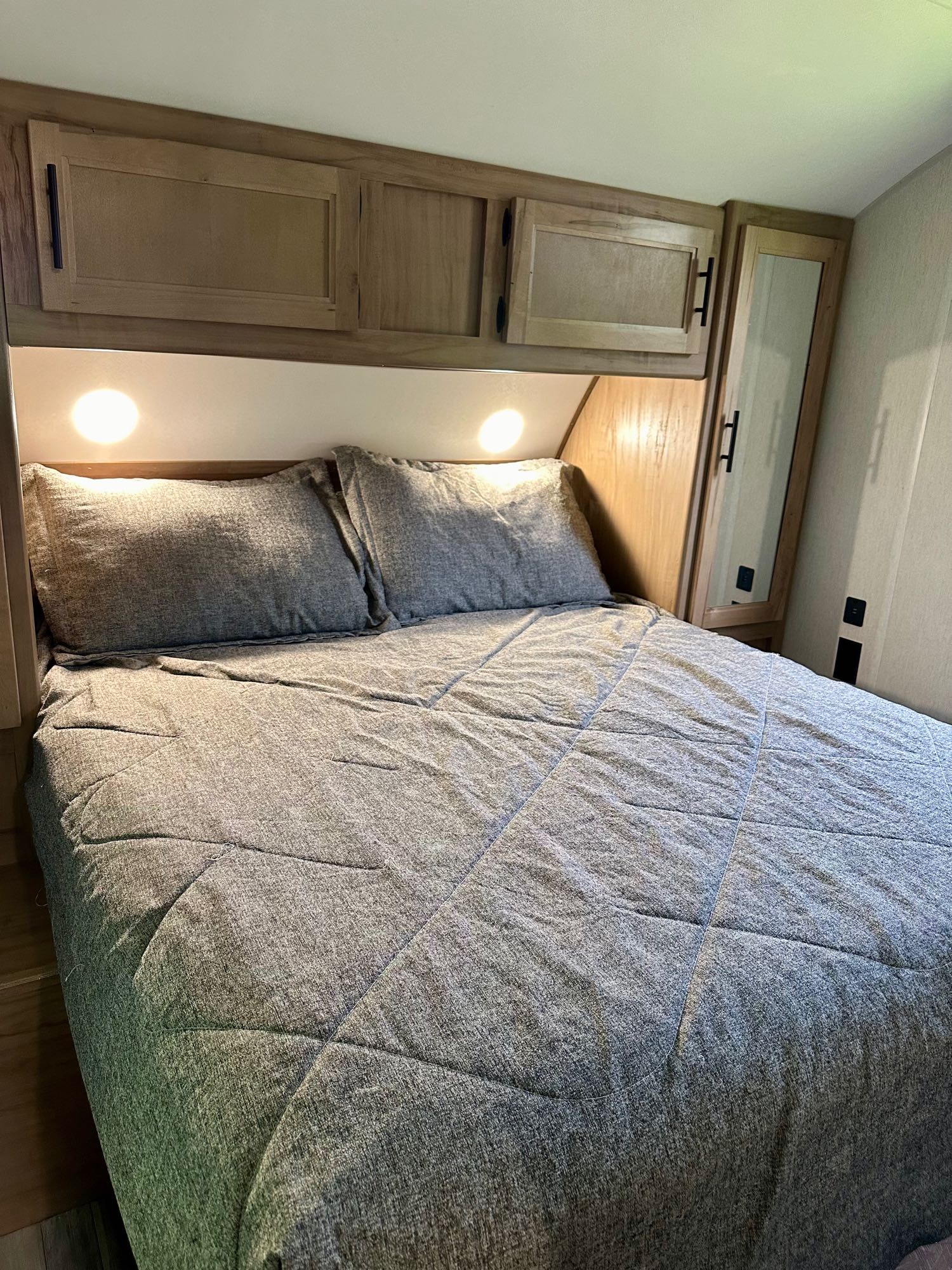 Cozy RV rental bedroom with gray quilted bedding, wall lights, and wooden overhead storage.. Forest River Cherokee Grey Wolf 2023