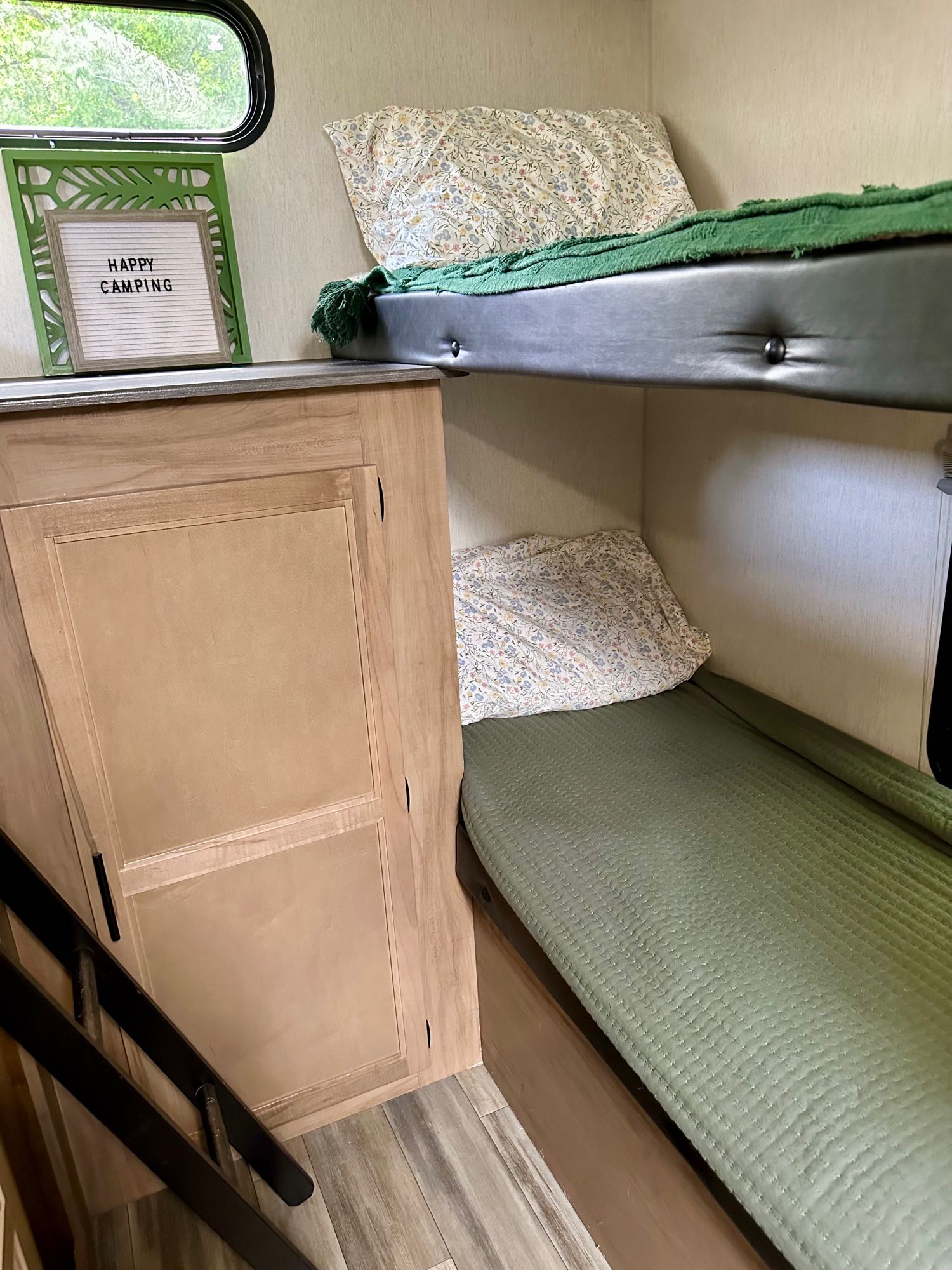 Cozy RV rental interior featuring stacked bunk beds with green and floral bedding, a ladder, and a "Happy Camping" sign.. Forest River Cherokee Grey Wolf 2023