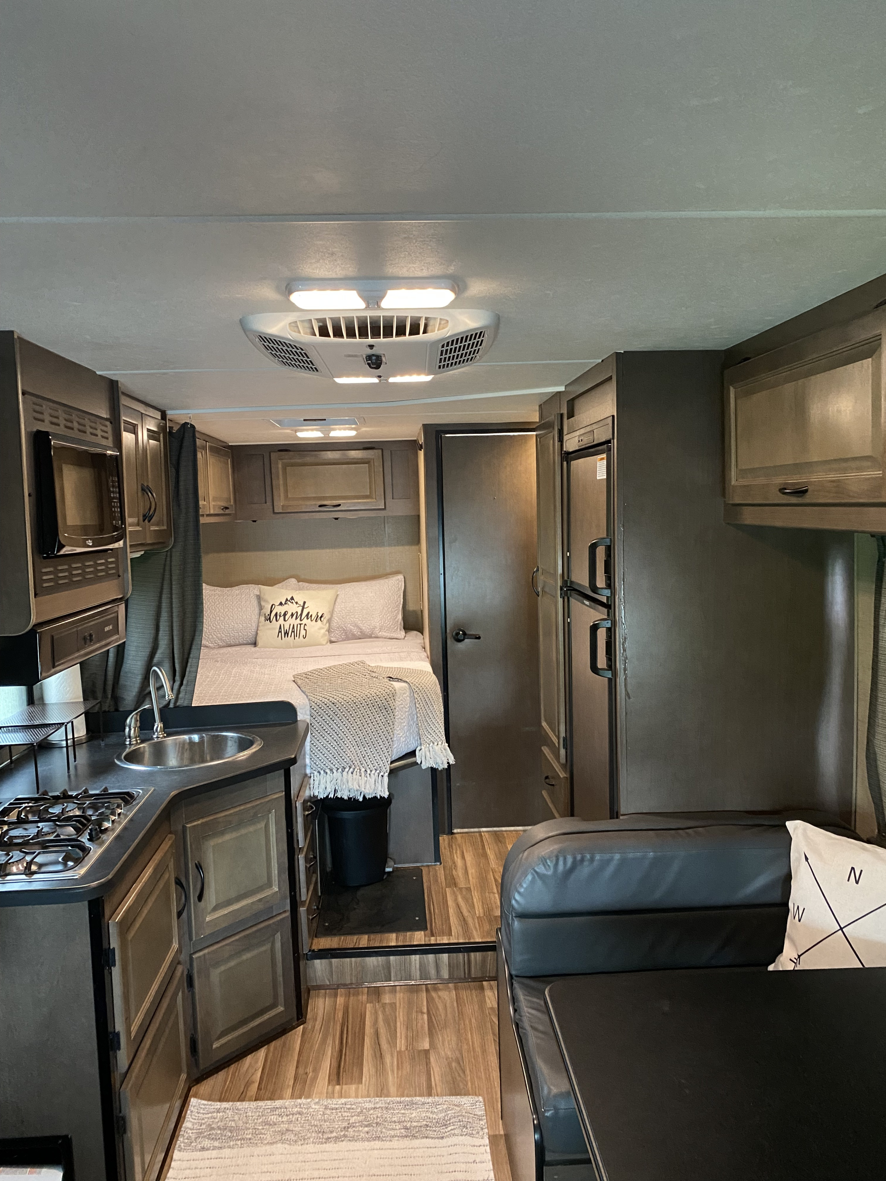 Cozy RV rental interior showcasing a compact kitchen, comfortable bed with an "adventure awaits" pillow, and dining area.. Thor Majestic 2019