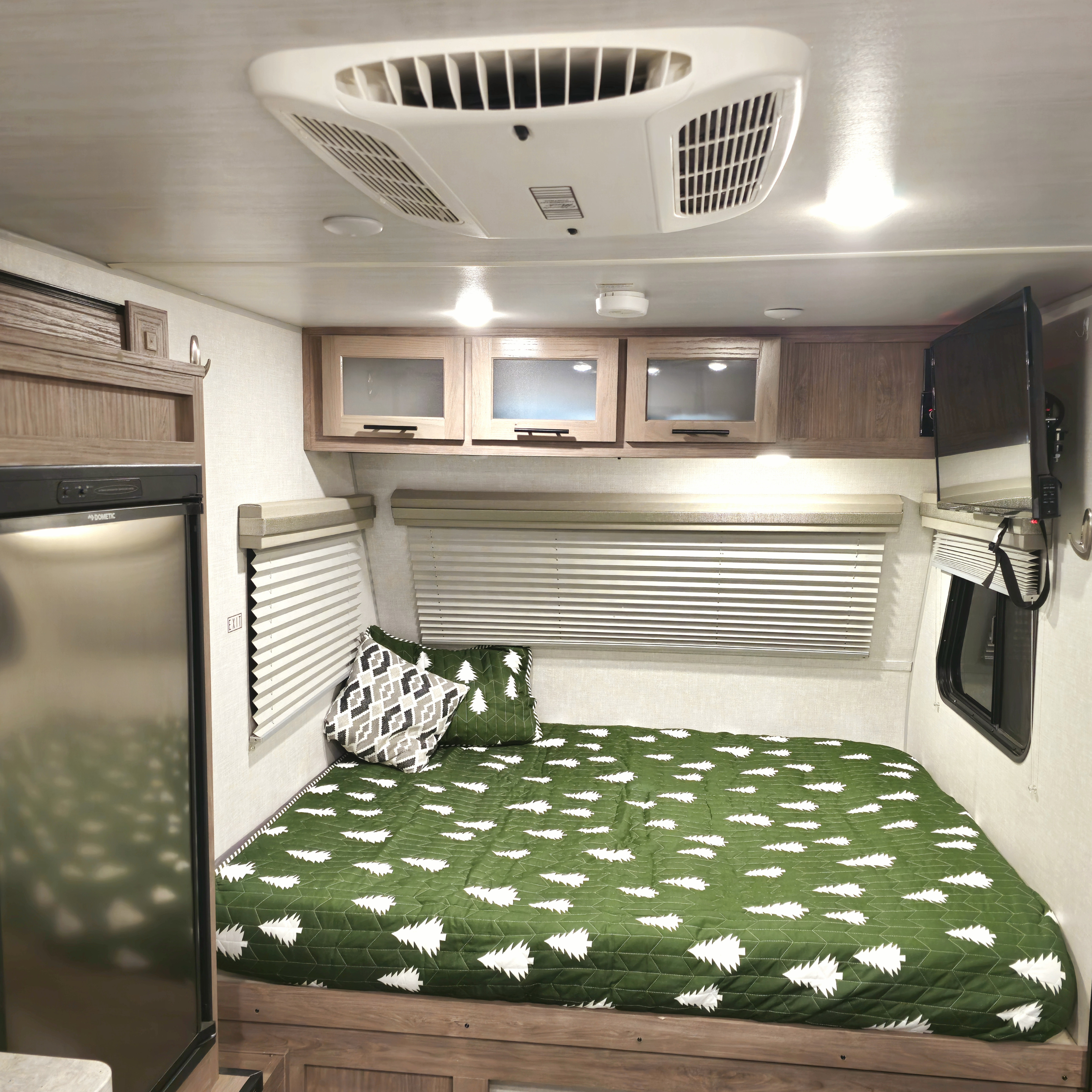 Explore this RV rental's bedroom: comfy bed with tree-patterned quilt, fridge, TV, & AC for your next journey.. No Boundaries 16.6 2021