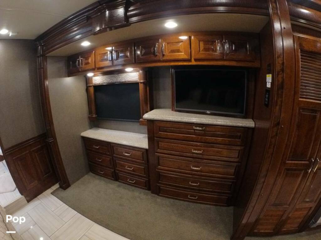 Luxury rv rental interior featuring dark wood cabinetry, dual built-in TVs, and a large dresser for storage.. American Coach Revolution 2017