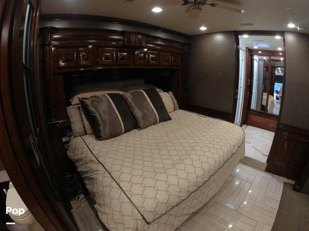 Spacious bedroom inside a luxurious RV rental, featuring a large bed, dark wood furniture, and bright lighting.. American Coach Revolution 2017