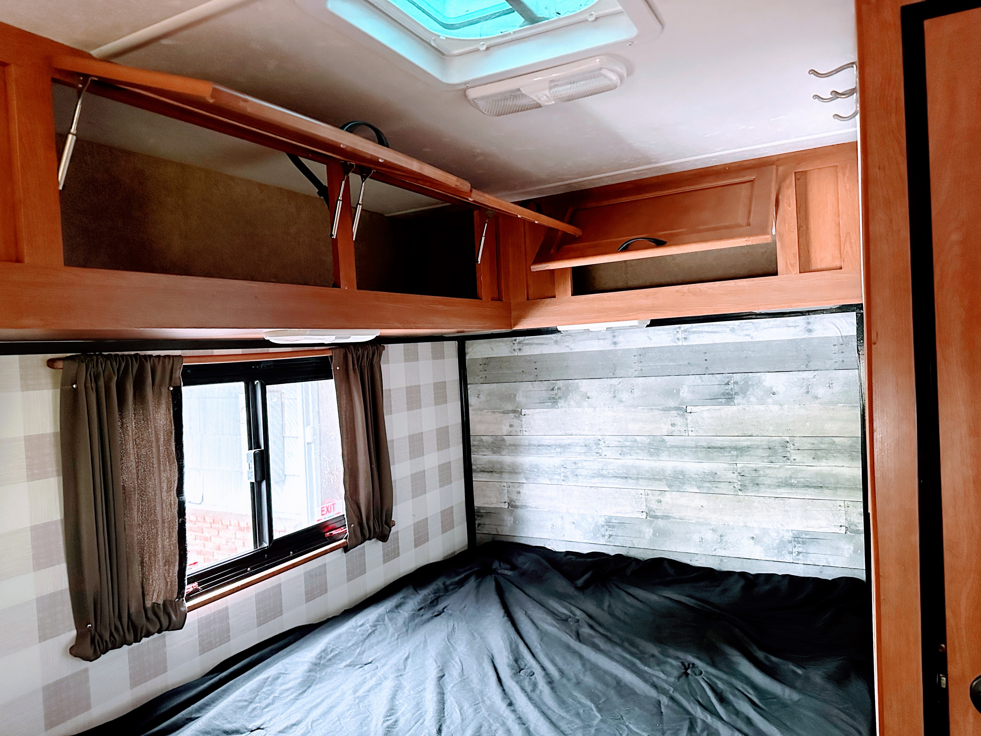 Inside an RV rental: a comfortable bedroom featuring open overhead cabinets, a window with curtains, and stylish wall panels.. Thor Majestic 2015