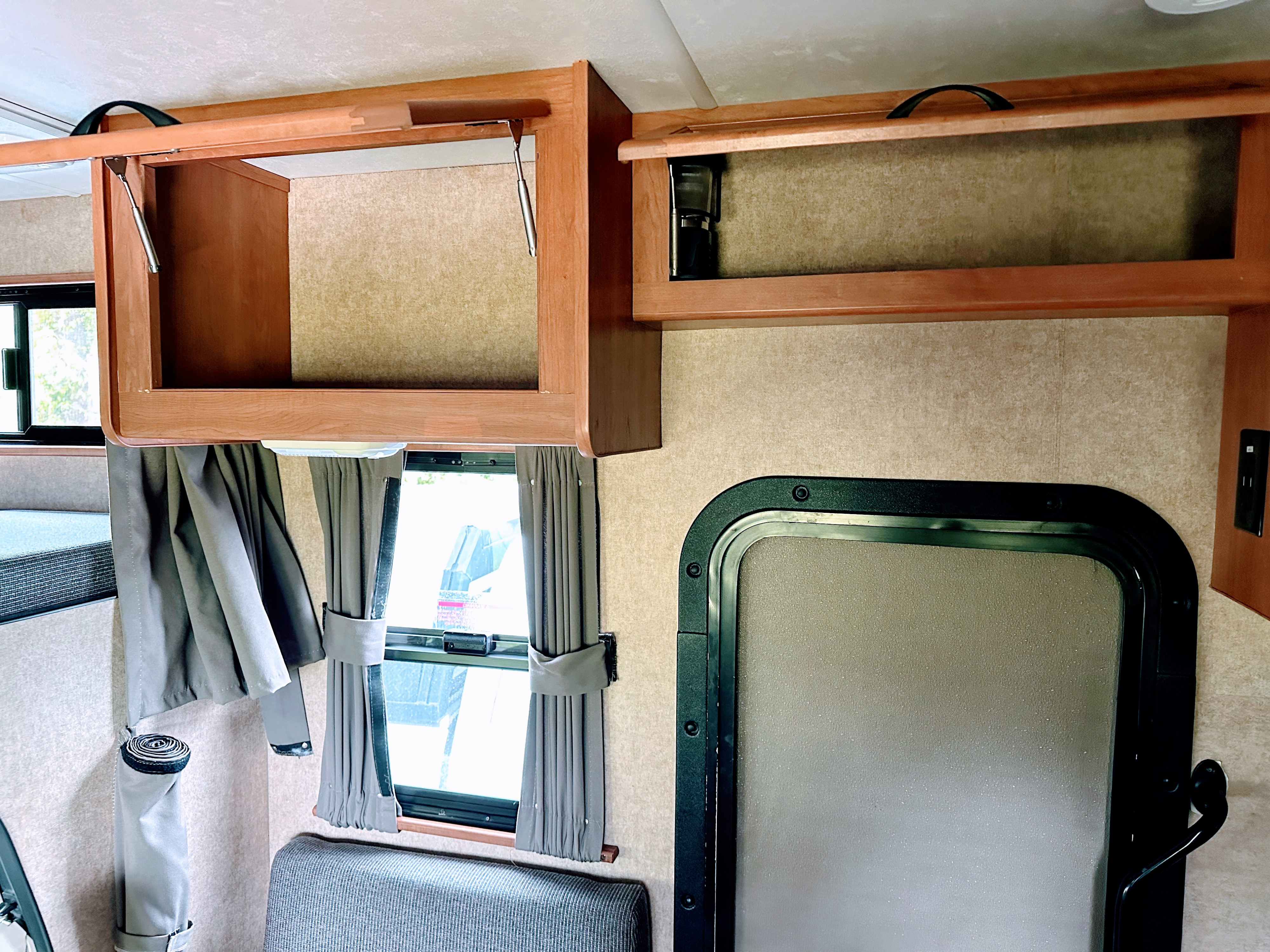 Interior of an RV rental with open overhead cabinets, a window with curtains, and a screen door, highlighting functional mobile living space.. Thor Majestic 2015