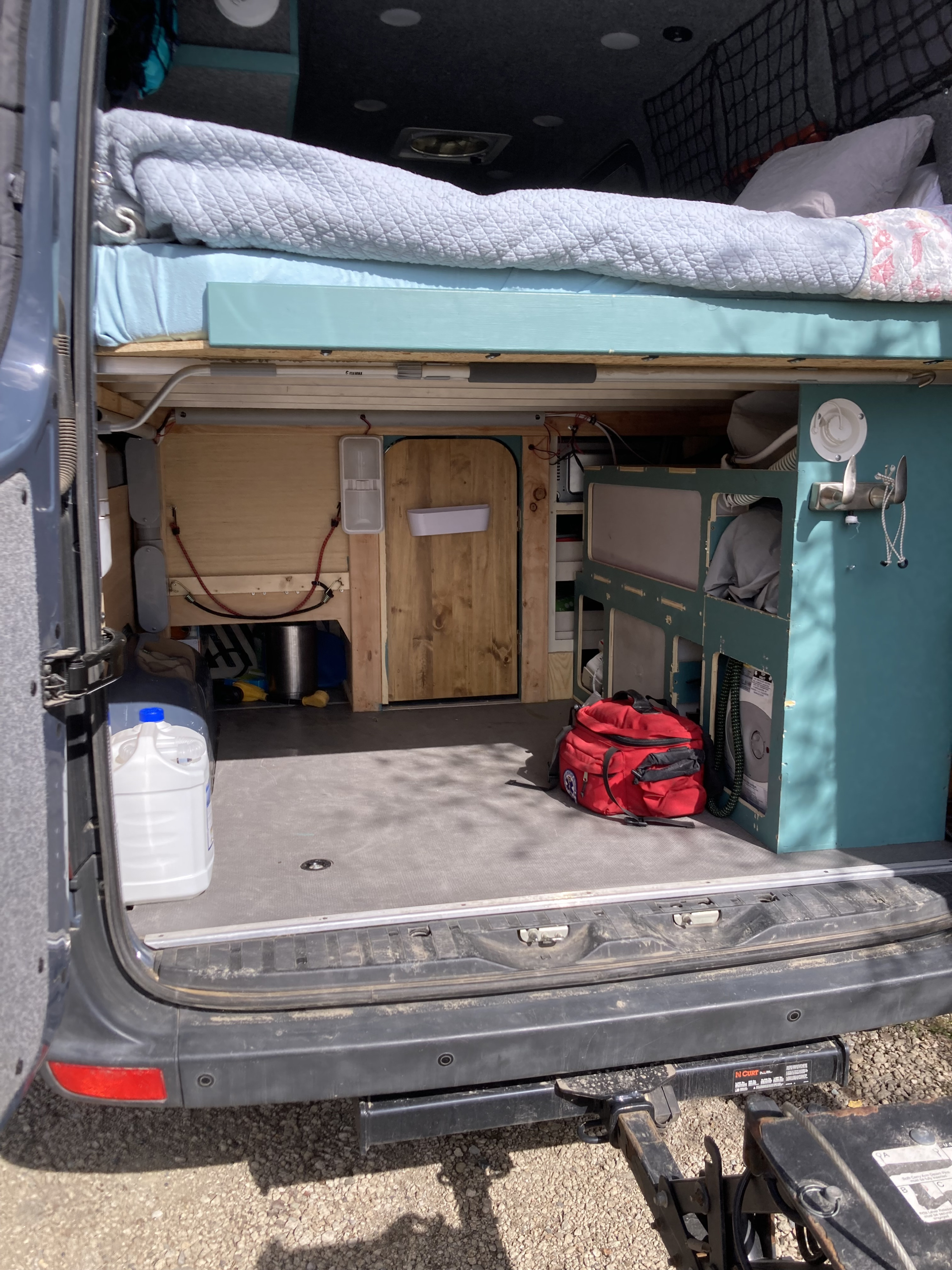 Inside an RV rental: a camper van's rear reveals an elevated bed, organized storage, and functional living space.. Mercedes Sprinter 2018