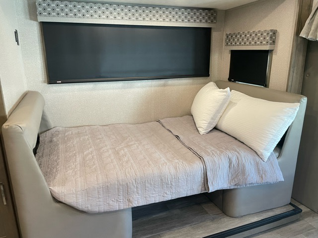 RV rental interior: a cozy convertible bed with pillows, windows with patterned valances, and light walls.. Forest River Dynamax Isata 3 24FW 2023