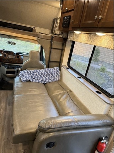 RV rental interior: Cozy living area with convertible sofa, overhead bunk bed, cabinets, window, & dashboard.. Forest River 3051S Ford 2017