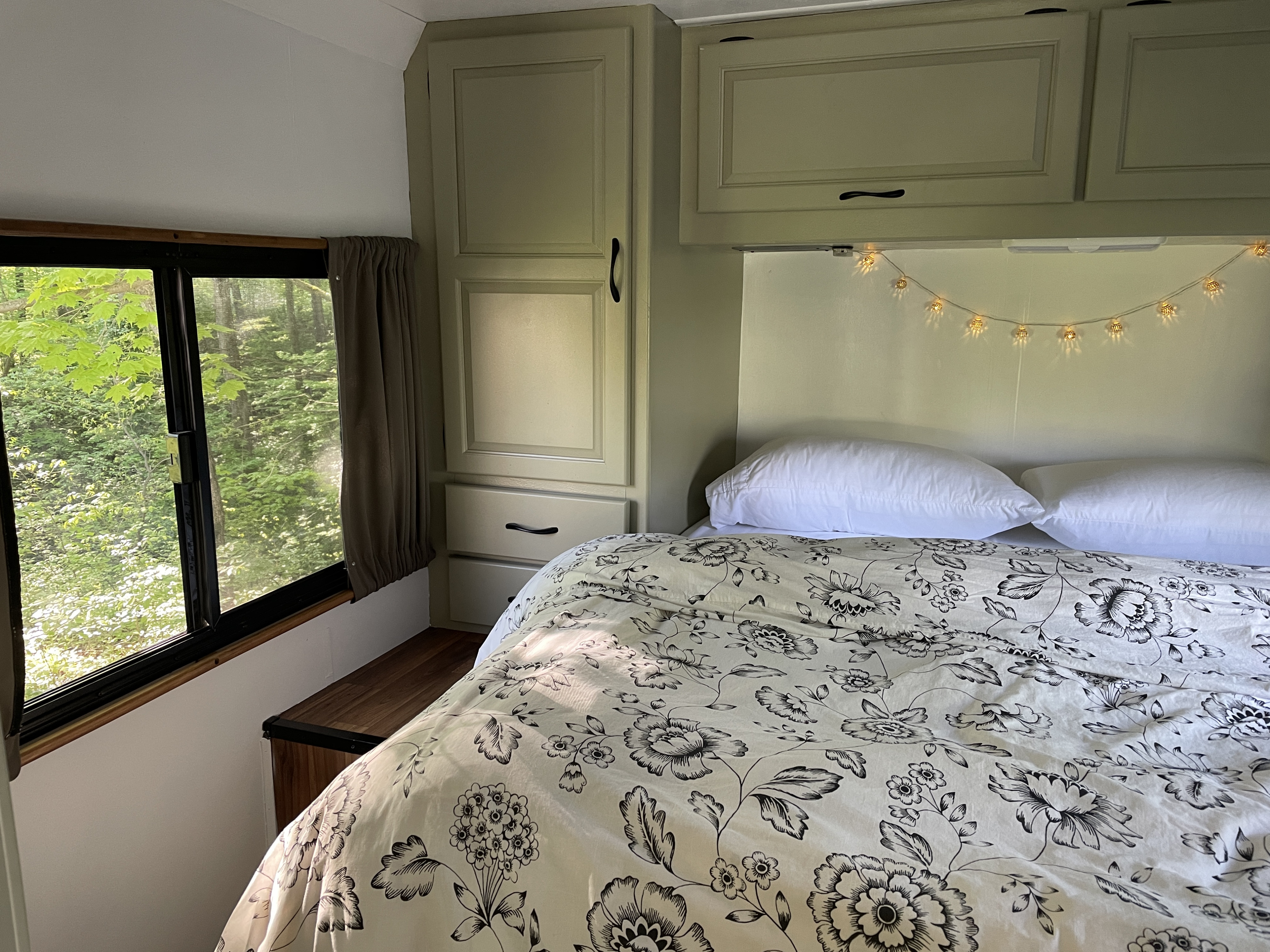 Cozy RV rental bedroom featuring a floral bedspread, nature view from the window, and warm string lights above the bed.. Thor Majestic 2015