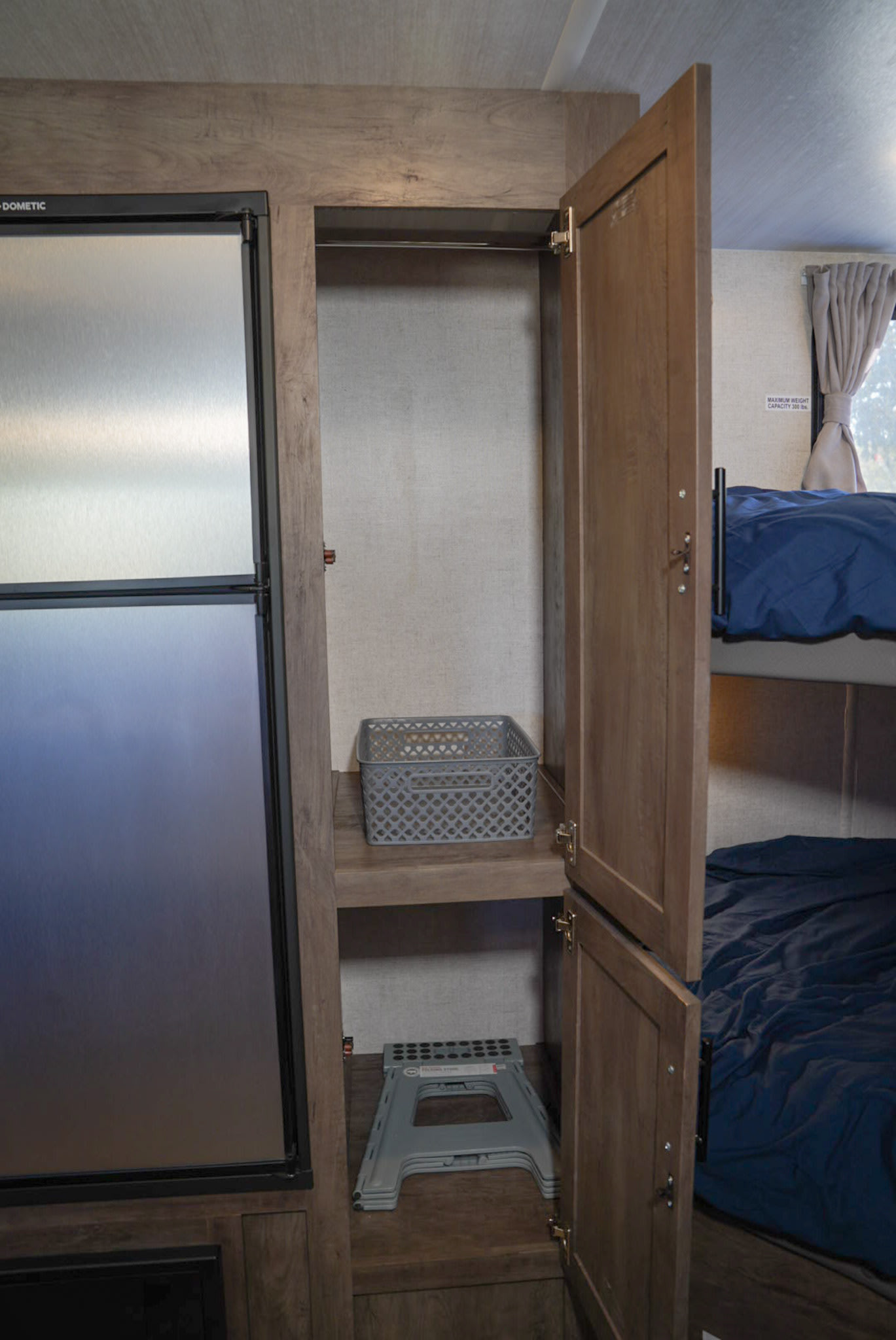 Inside an RV rental: a Dometic refrigerator, open wardrobe with a step stool, and bunk beds are visible.. Forest River EVO 2021