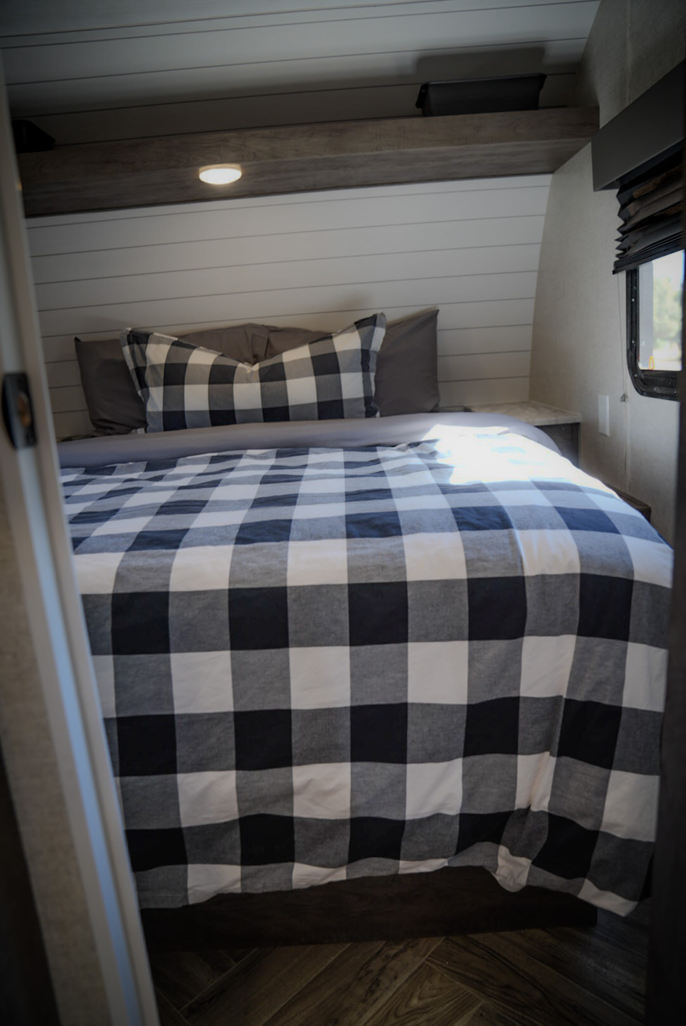 Cozy RV rental bedroom with black & white buffalo plaid bedding, shiplap walls, built-in light & window.. Forest River EVO 2021