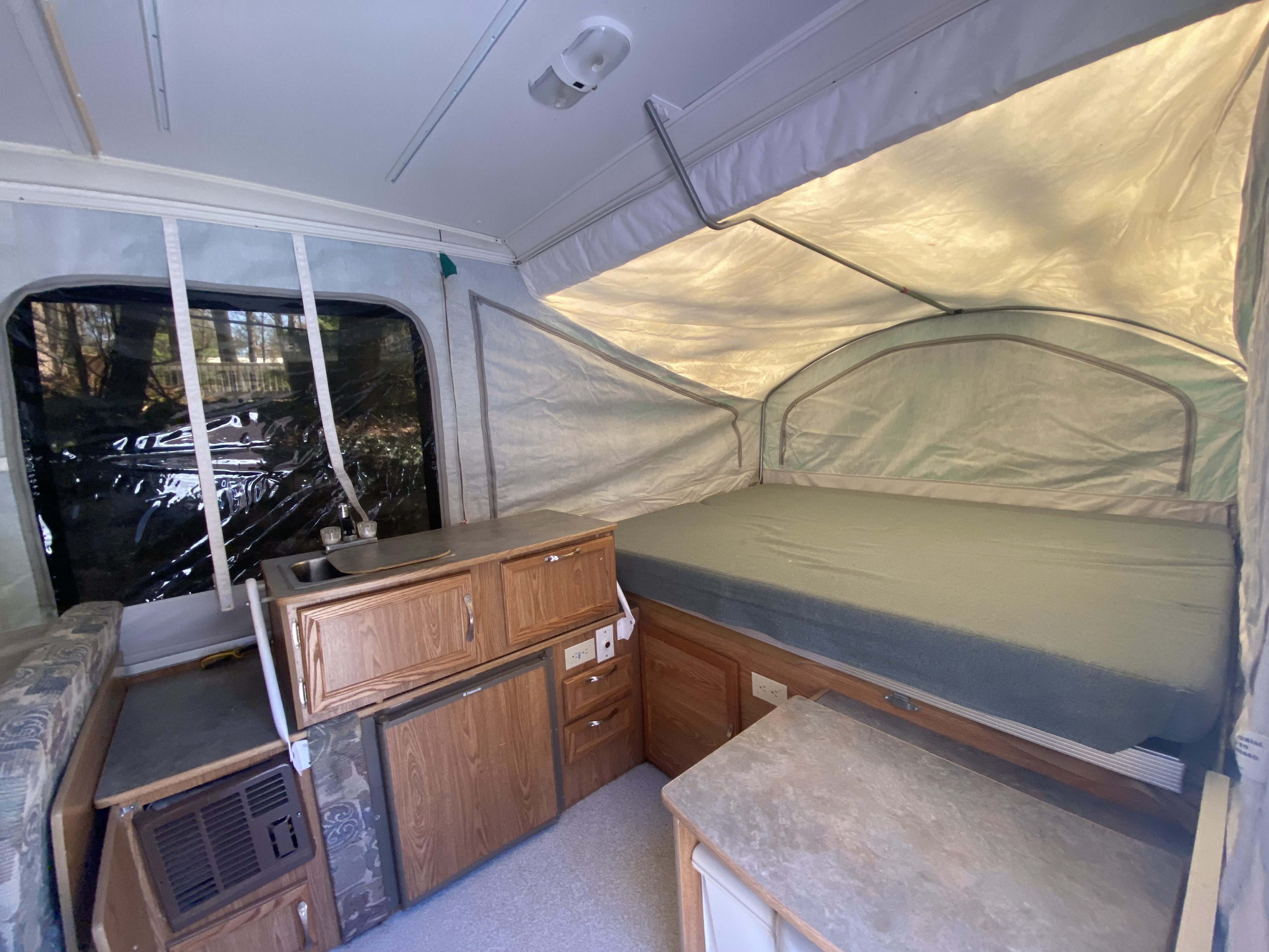 Interior of an RV rental pop-up camper, featuring a bed, kitchenette with sink, and seating. Ideal for compact travel.. Coachmen Clipper 2004