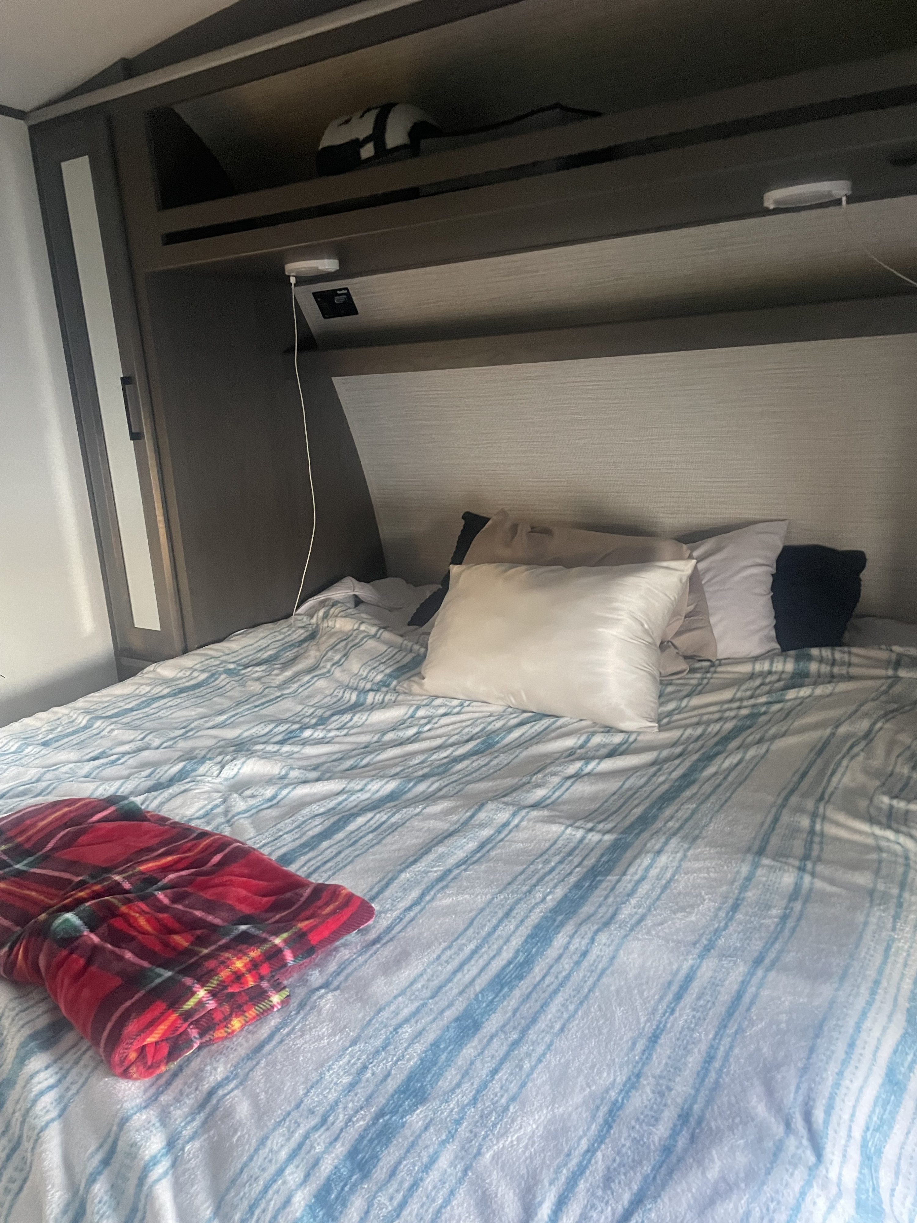Inside this RV rental bedroom: a comfy bed with blue striped bedding, varied pillows, and compact overhead storage.. Heartland 265 2021