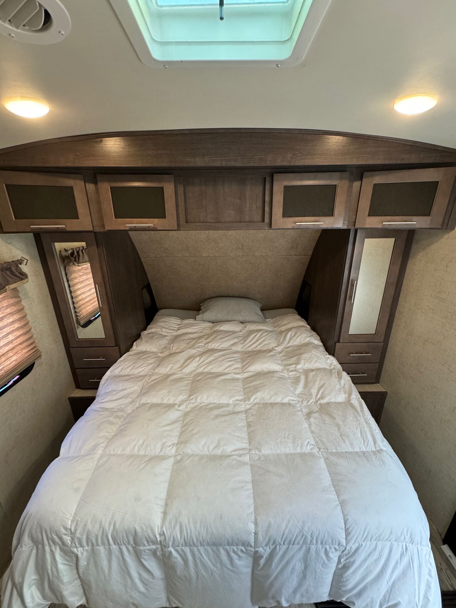 Cozy RV rental bedroom with a comfy bed, overhead cabinets, and mirrored side wardrobes.. Forest River Surveyor 2015