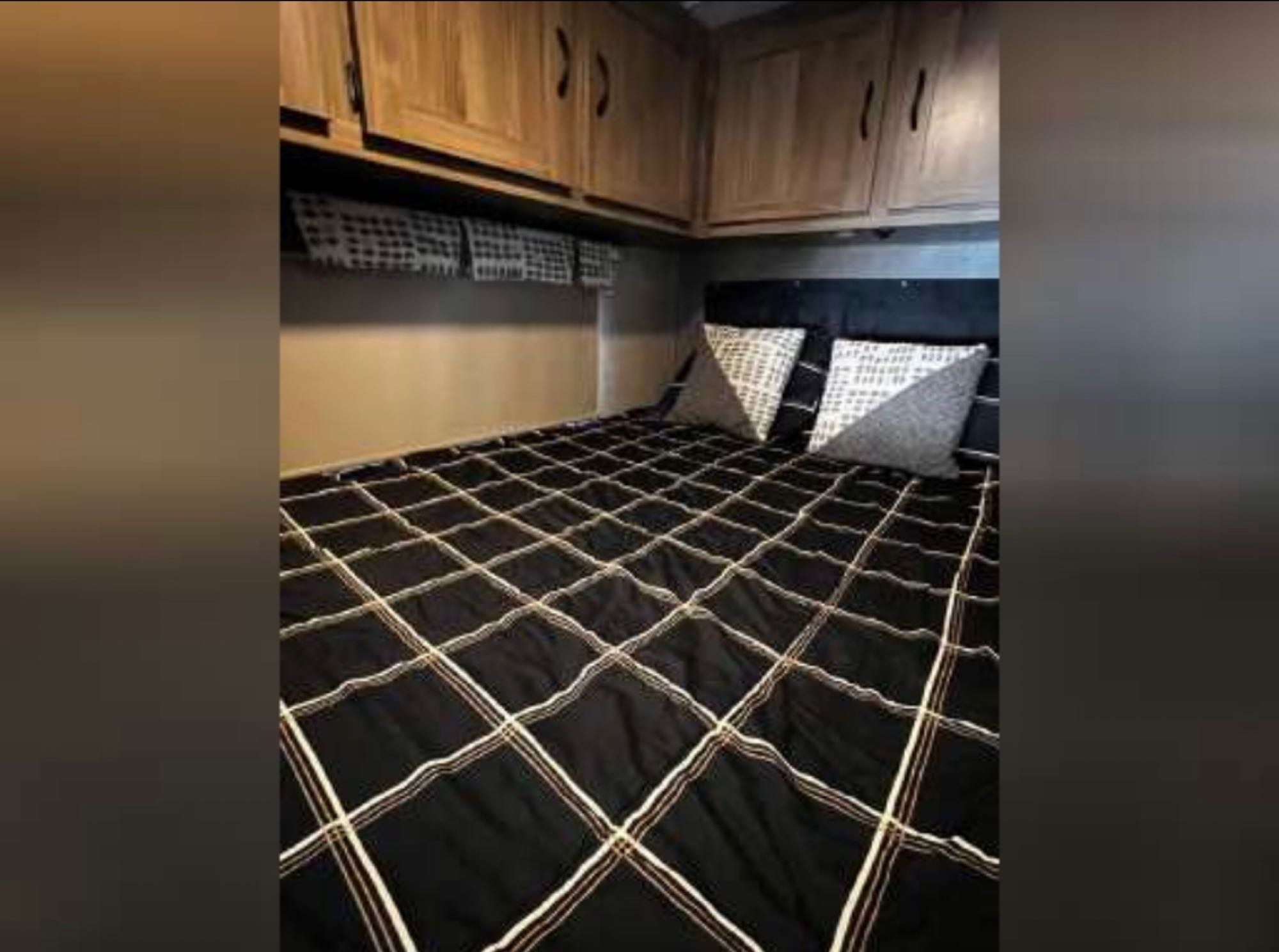 Comfortable RV rental bedroom with a black patterned comforter, decorative pillows, and wooden overhead storage cabinets. Perfect for trips.. Coachmen Prism 2016