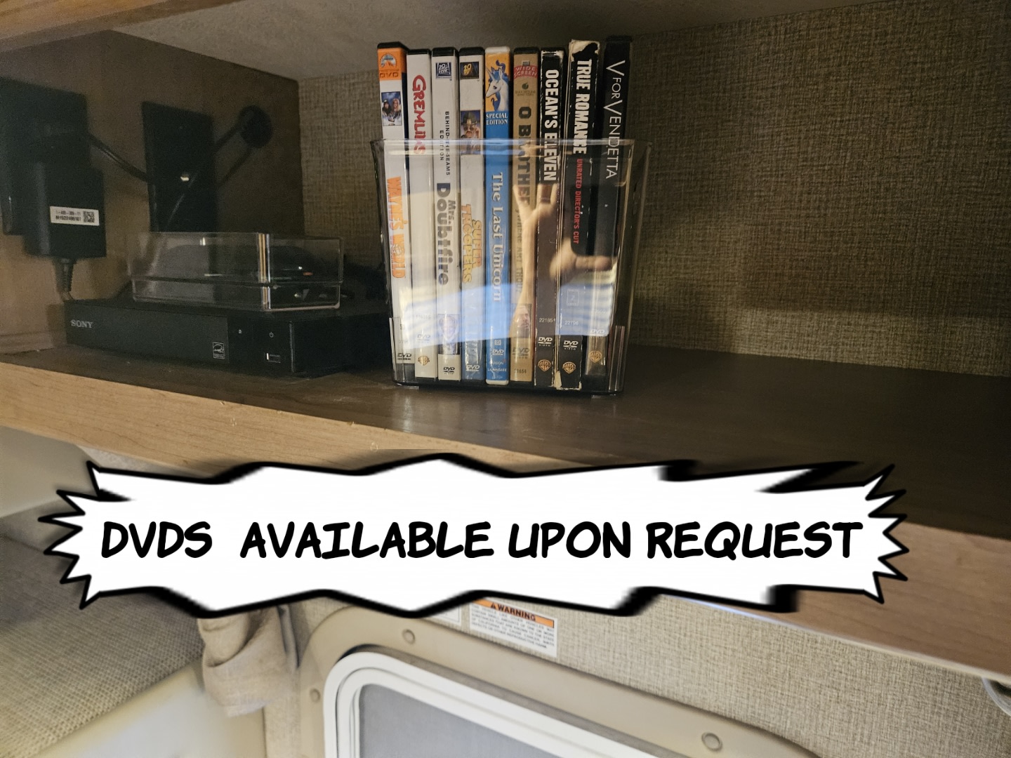 RV rental entertainment: A shelf in an RV with a Sony DVD player and a collection of movies, available upon request.. Thor Motor Coach Four Winds 2021