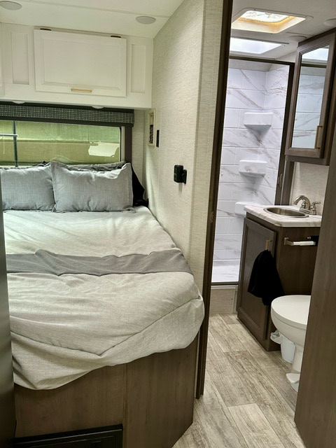 RV rental interior showing a cozy bedroom with overhead cabinets and an adjacent compact bathroom with shower & toilet.. Thor Chateau 2024