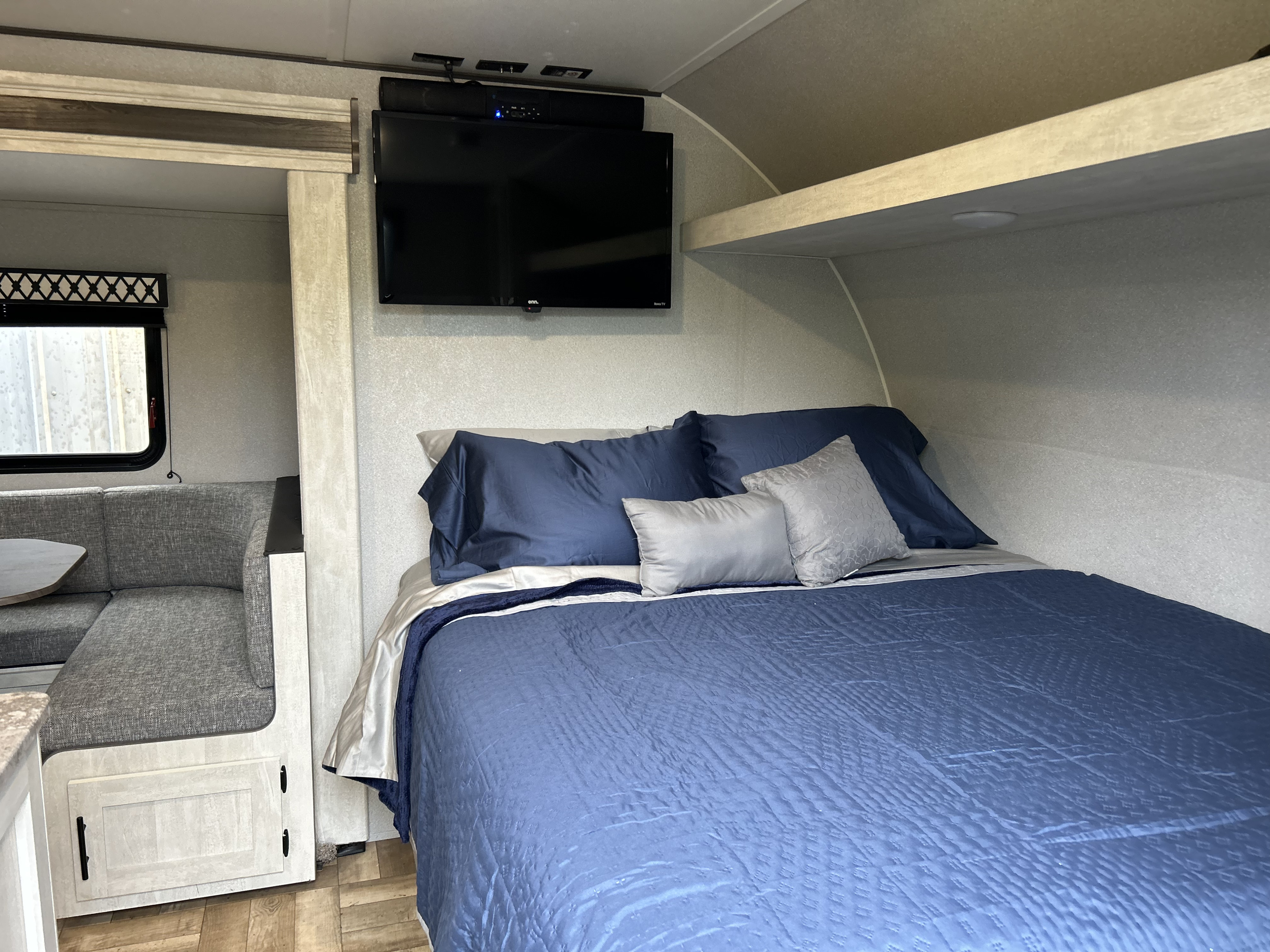 Cozy RV rental bedroom featuring a bed with blue and gray bedding, a mounted TV, and an adjacent dinette area.. Forest River Shasta 2023