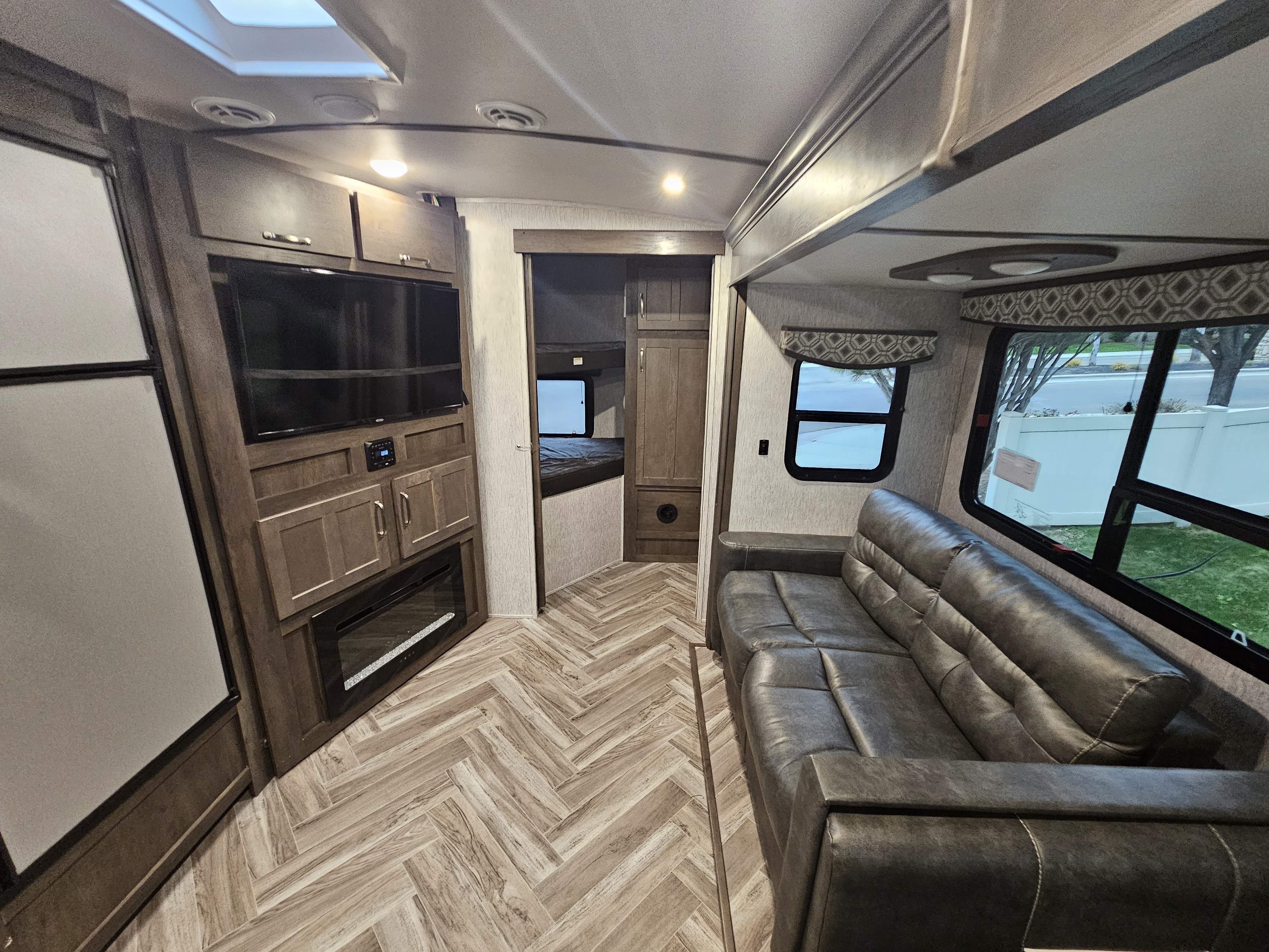 Step inside this RV rental's modern living space: A large sofa, entertainment center, fireplace, wood-look herringbone floor, and rear bunk room.. Dutchmen Astoria 2903BH 2021
