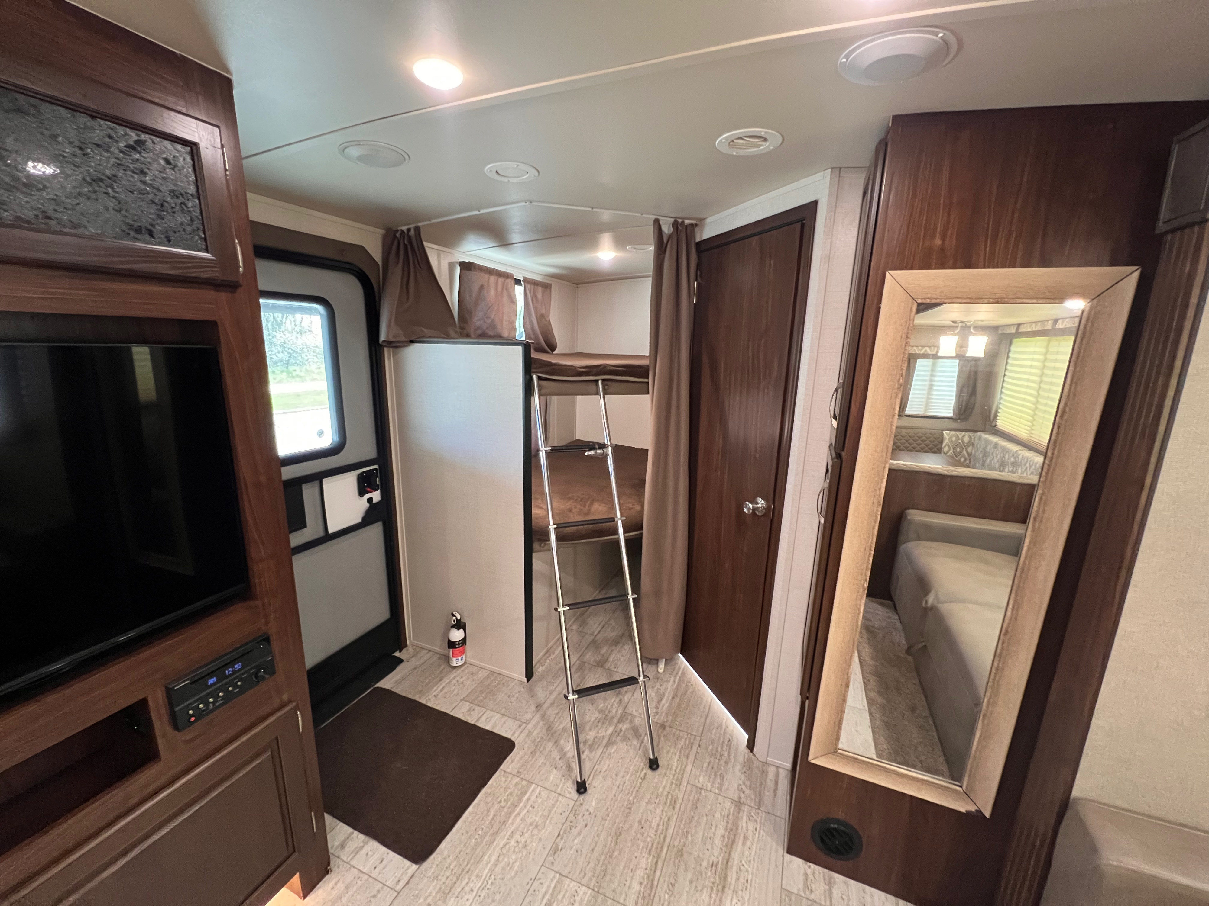 RV rental's inviting interior: bunk beds, entertainment unit, and a mirror revealing the dinette. Cozy travel space.. Forest River Solaire 2020