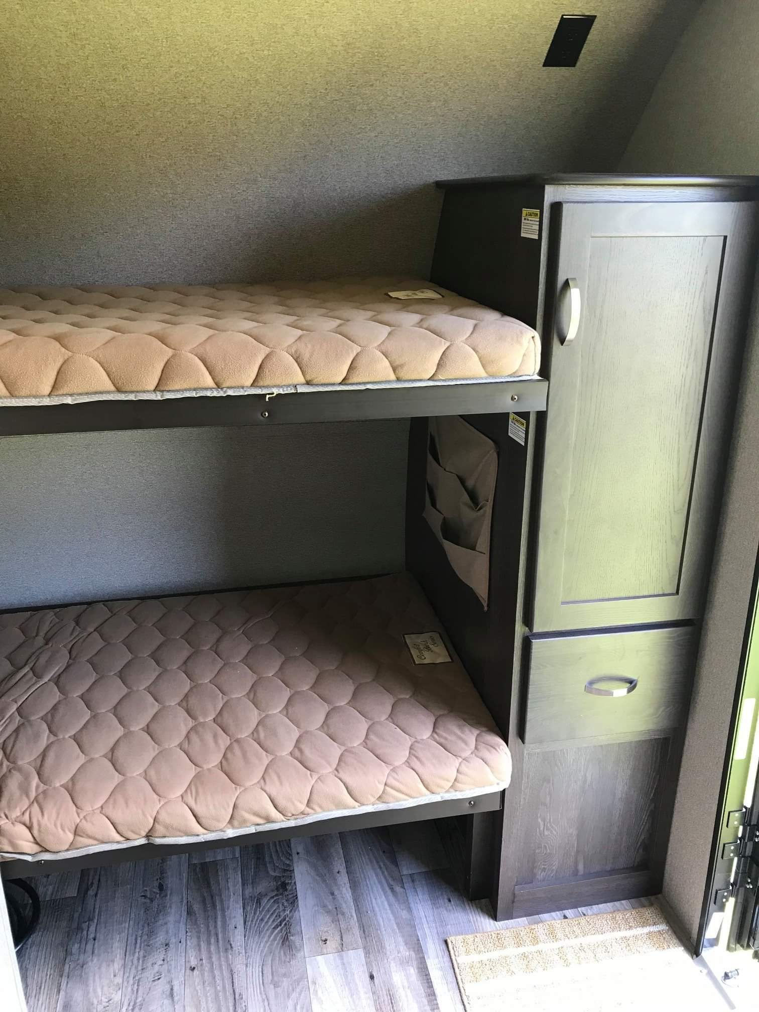 RV rental interior featuring two bunk beds with quilted mattresses, a built-in wardrobe, and light wood plank flooring.. Keystone RV Outback 210URS 2018