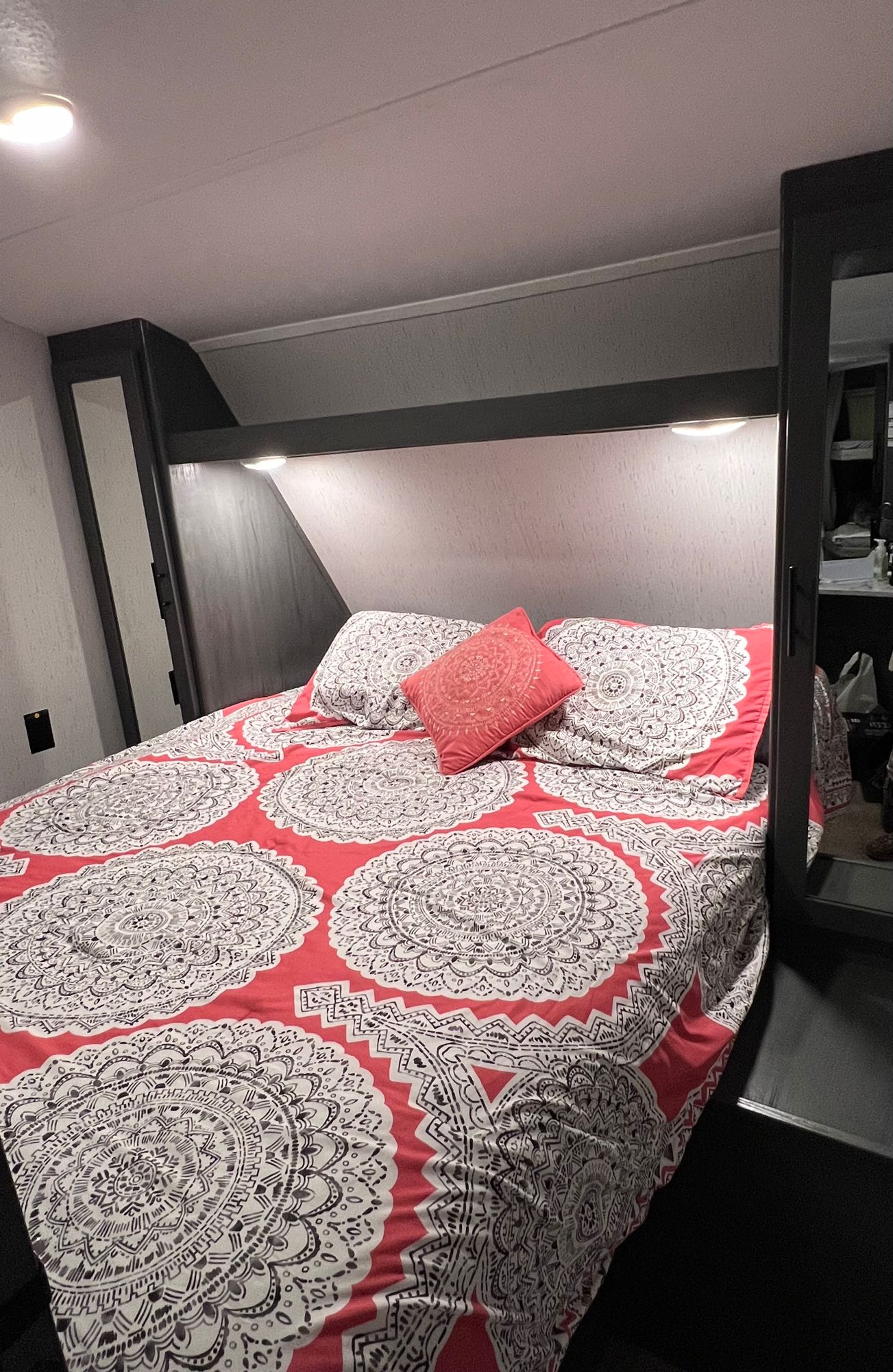 Cozy RV rental bedroom featuring a comfy bed with a red and white patterned comforter and reading lights.. Dutchman 26BHCWE 2024