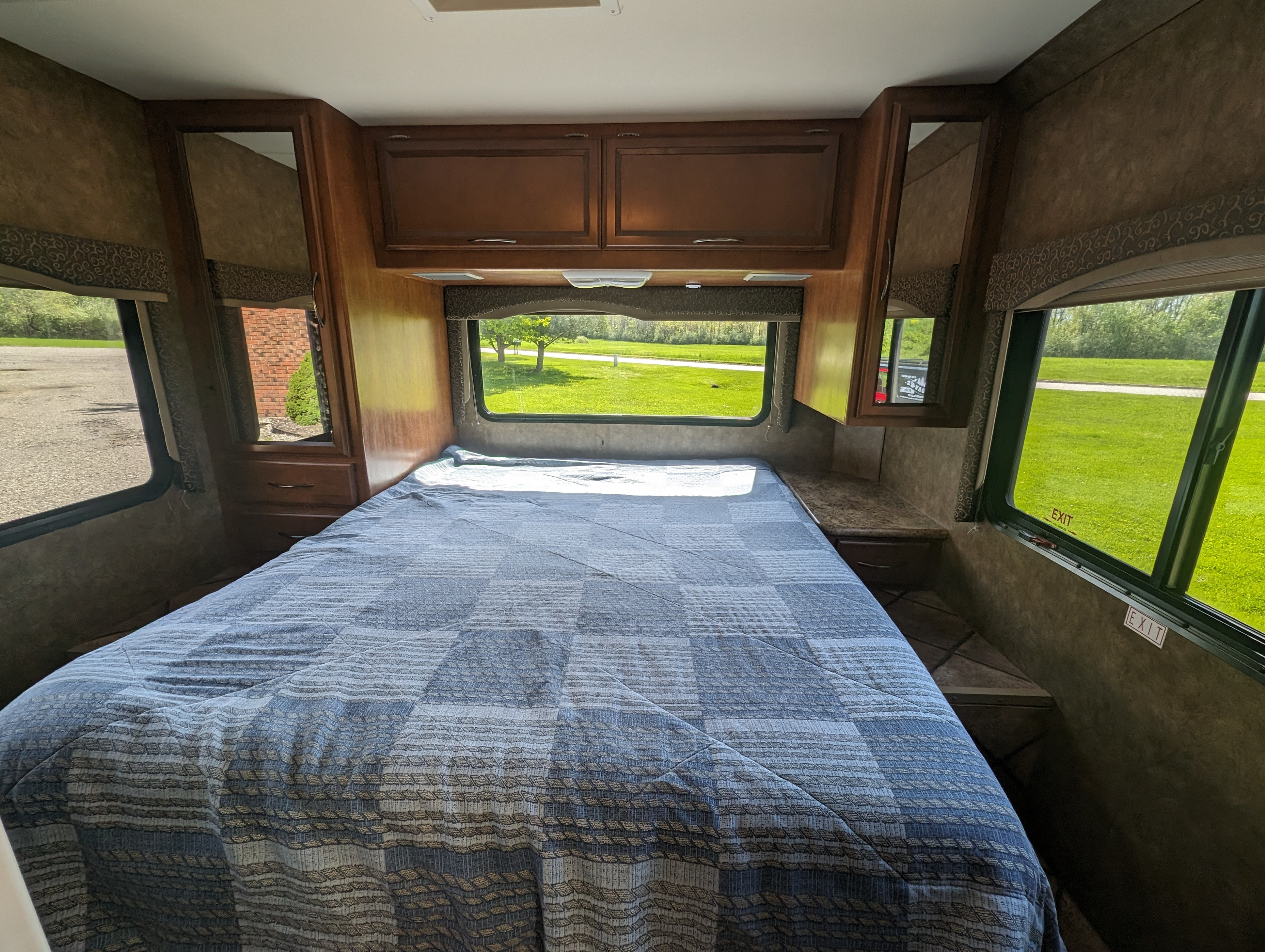 Spacious RV rental bedroom featuring a cozy bed, overhead cabinets, and bright windows looking out to nature.. Thor Motor Coach Four Winds 2014