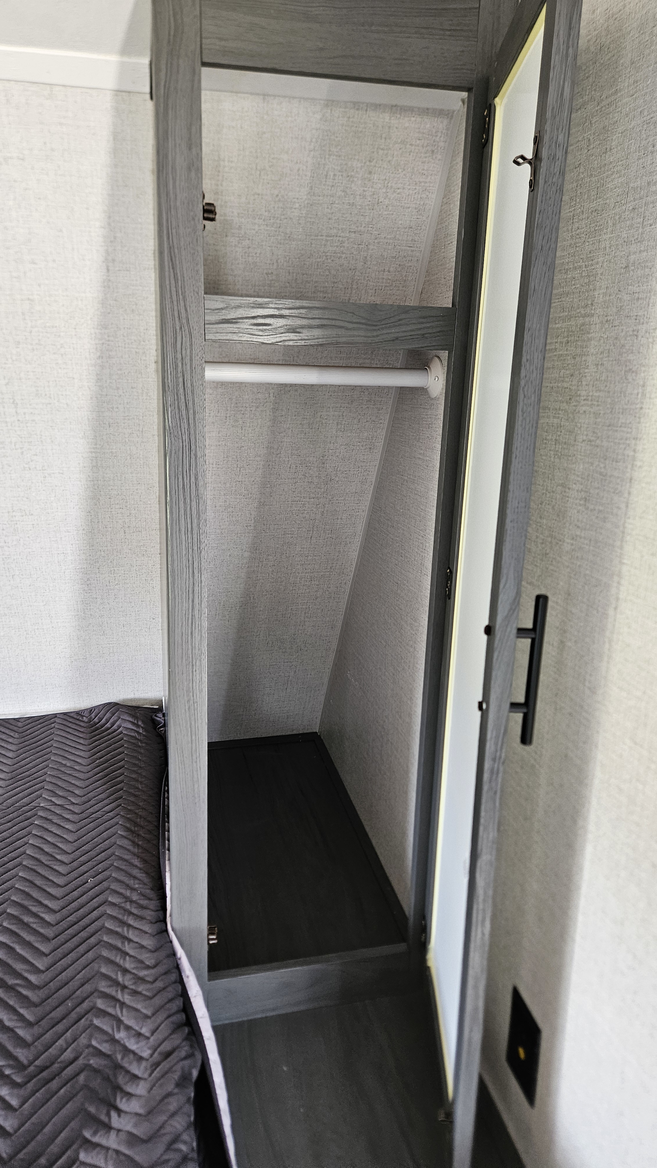 RV rental bedroom: Open closet with hanging rod and lower shelf for clothes, next to a bed with dark quilt.. Aspen Trail LE 2022