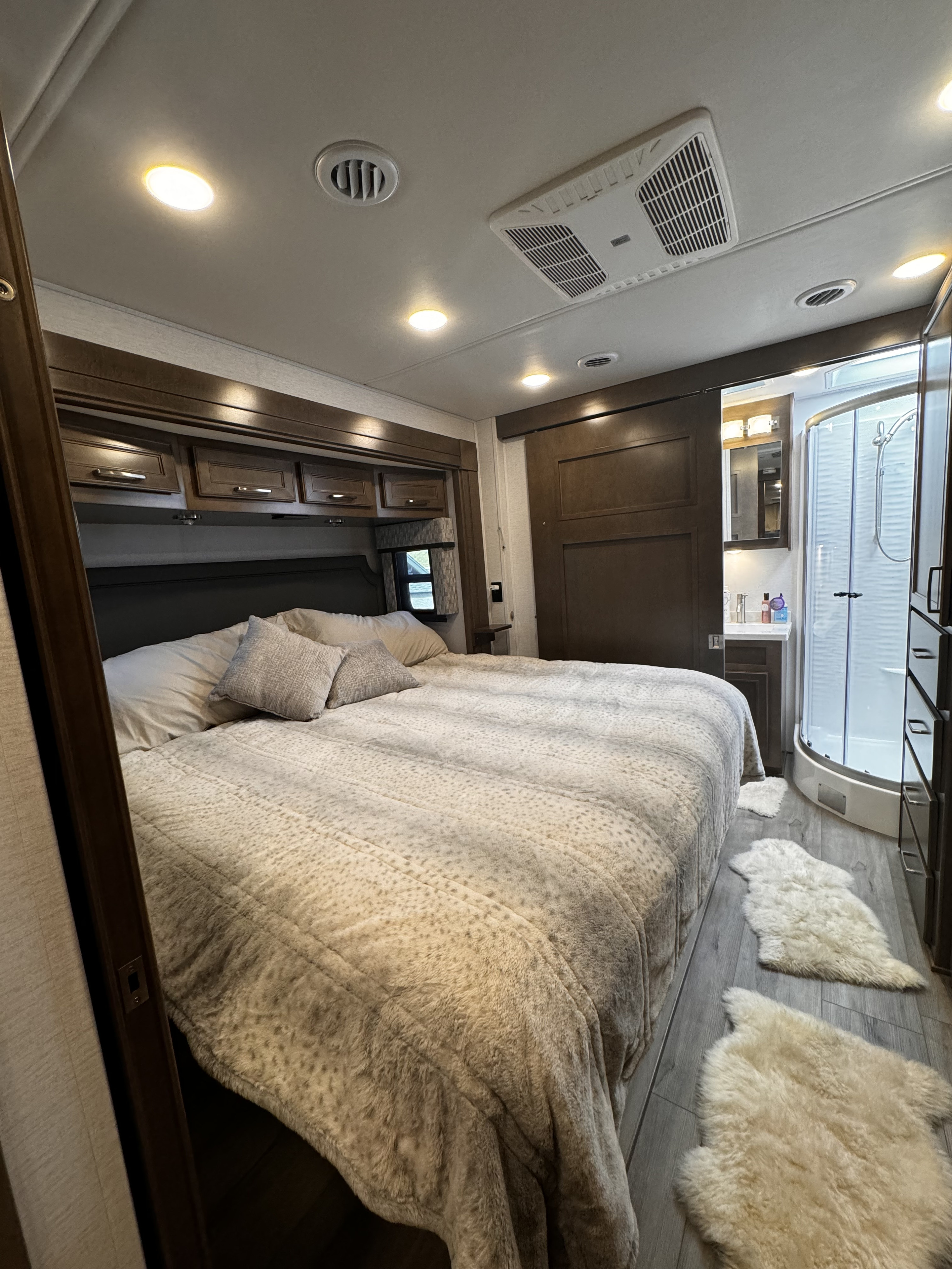 Comfortable RV rental bedroom featuring a large bed, overhead storage, and an attached compact bathroom with shower.. Renegade Verona 40 VRB 2024