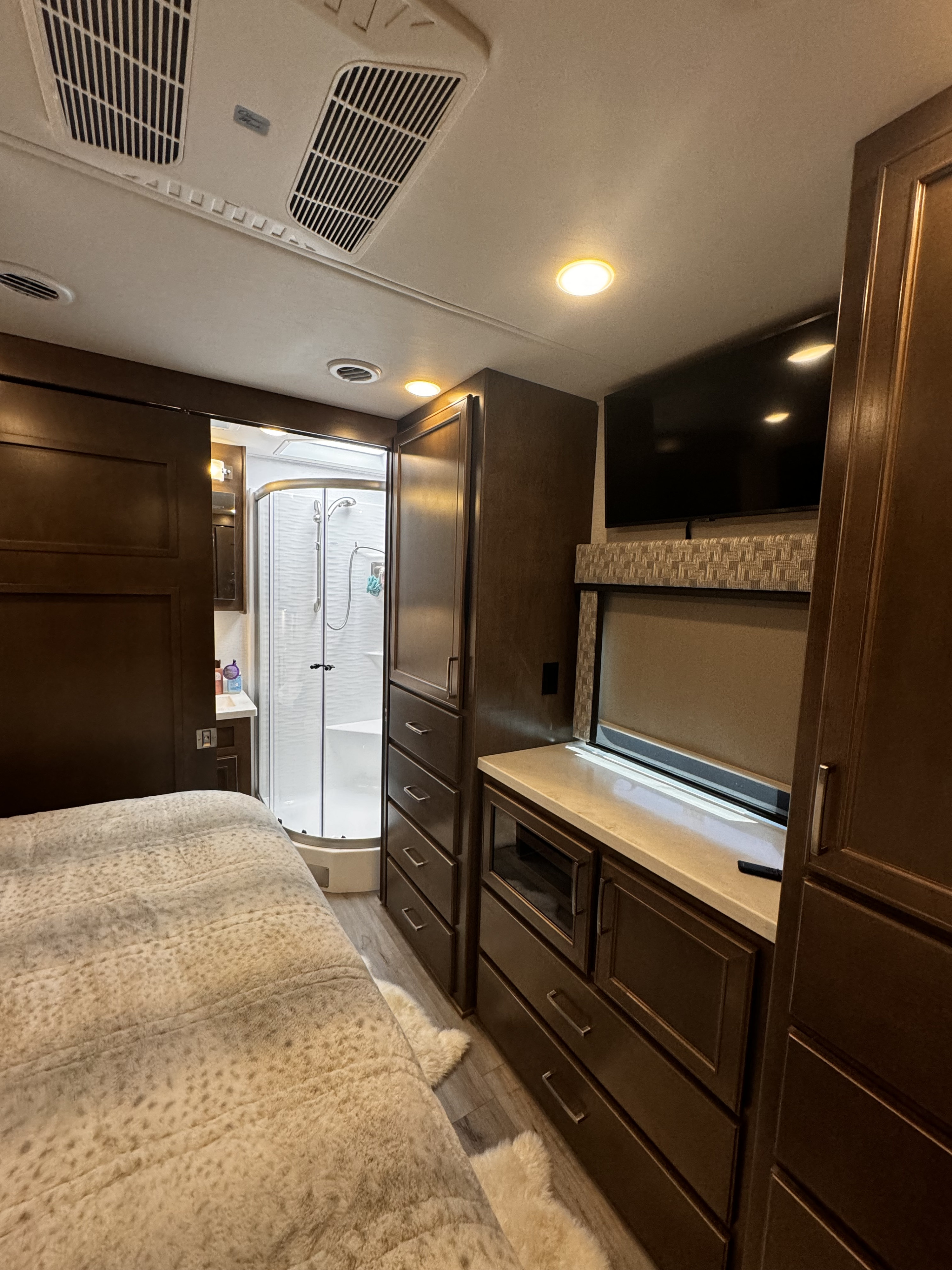 Experience comfort in this RV rental bedroom with a cozy bed, adjacent compact bathroom with shower, integrated storage, and TV.. Renegade Verona 40 VRB 2024