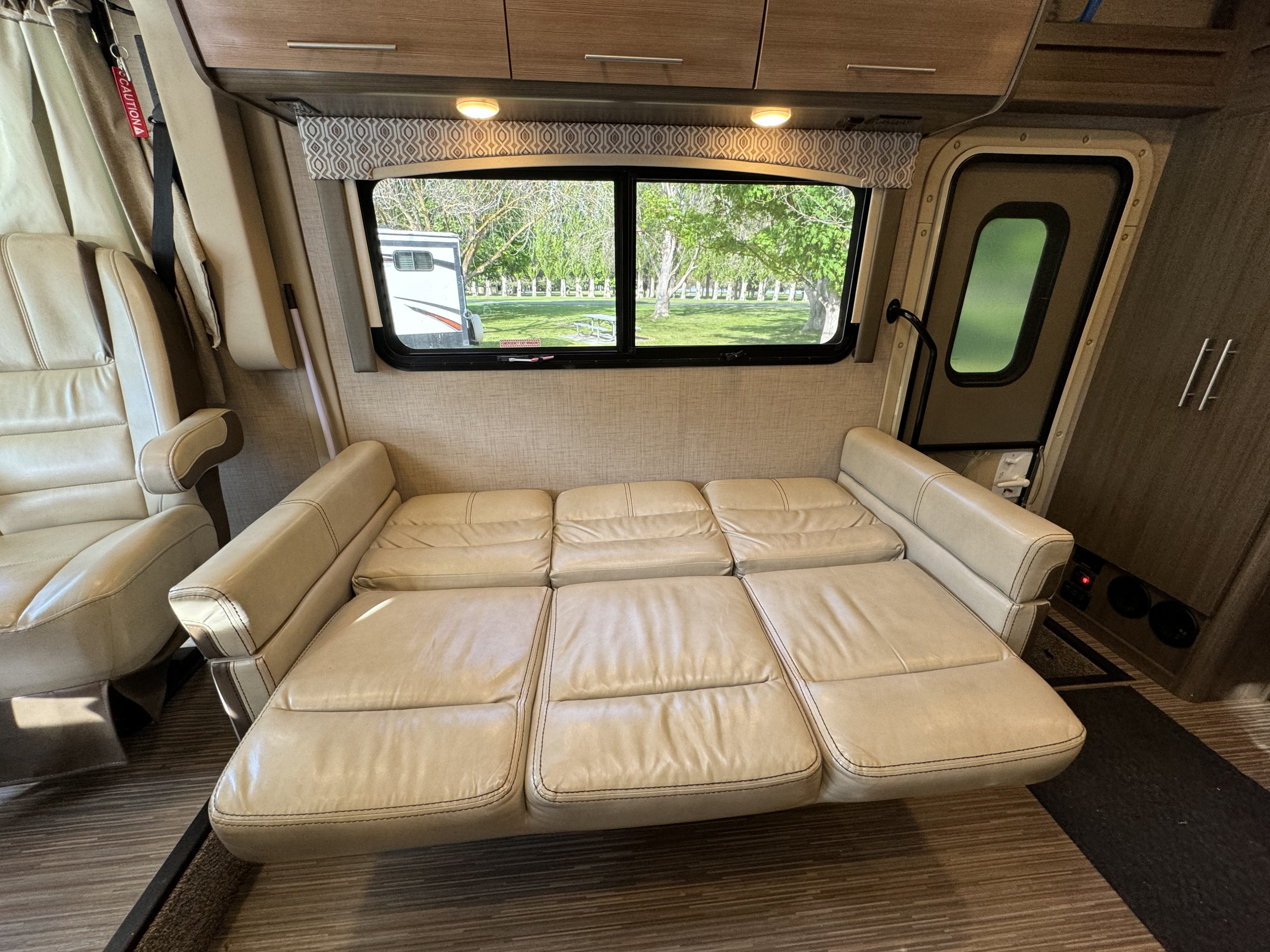 Inside a cozy RV rental: light beige convertible sofa, passenger seat, and scenic window view.. Thor Vegas 2018